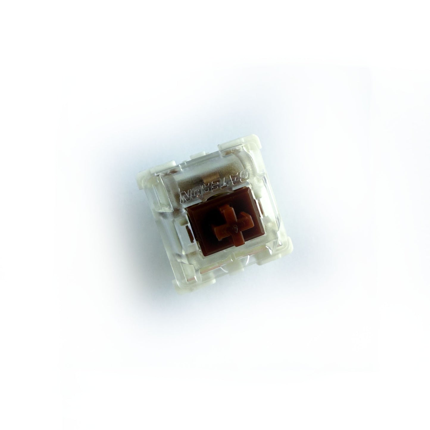 A tactile keyboard switch on a white background. The switch component is brown, the bottom of the casing is white, and the top of the casing is clear with the word "GATERON" imprinted into it.