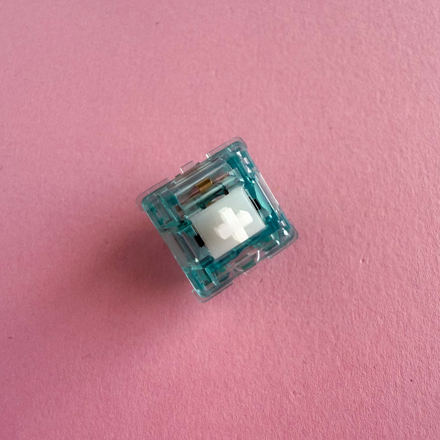 A tactile keyboard switch on a pink background. The switch component is white, and the casing is a translucent blue.