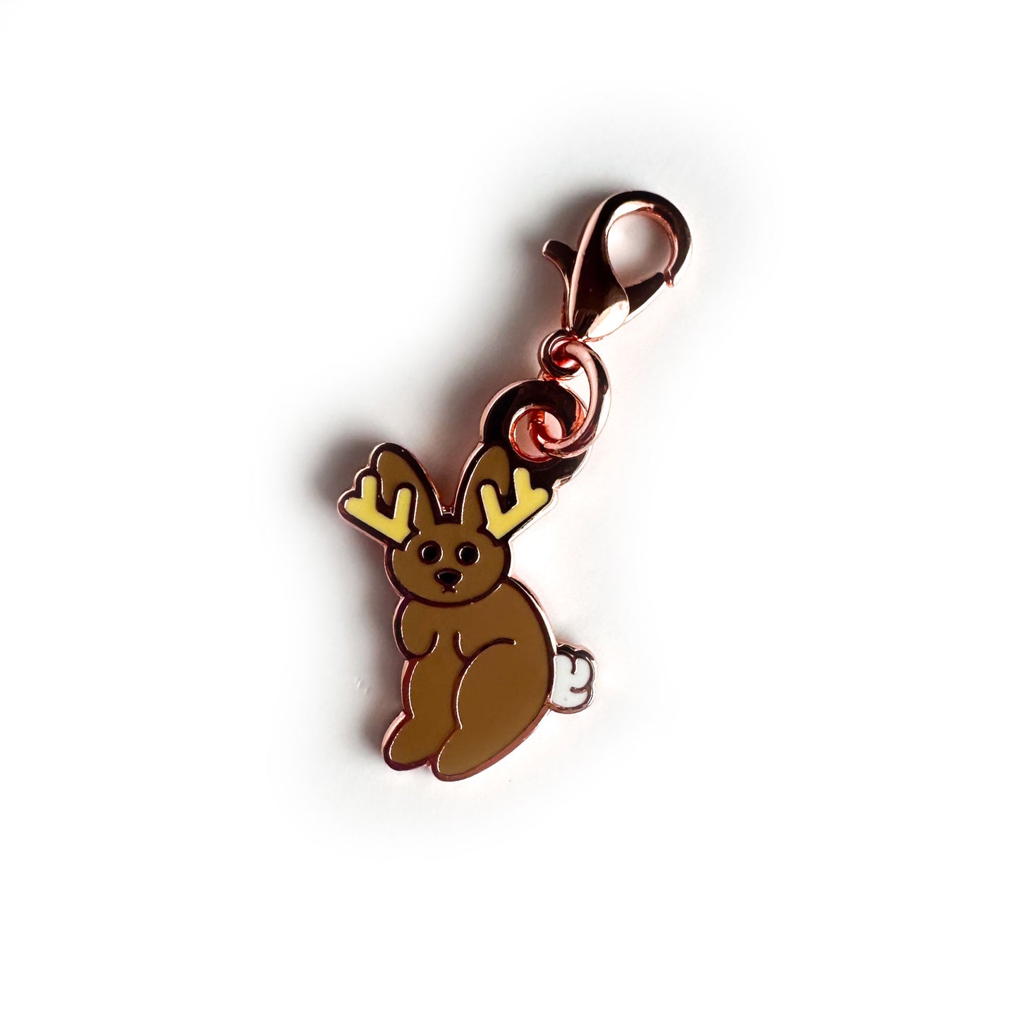 An enamel charm with a lobster claw clasp in the shape of a jackalope, it is in a cute stylized cartoon style.