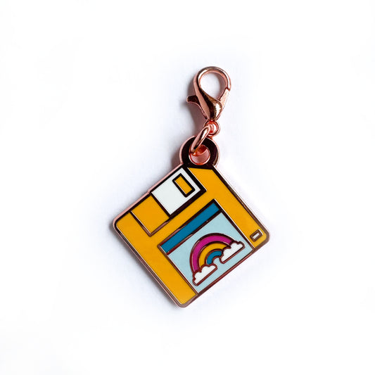 A lobster claw clasp charm shaped like a yellow floppy disk with a rainbow on the label.