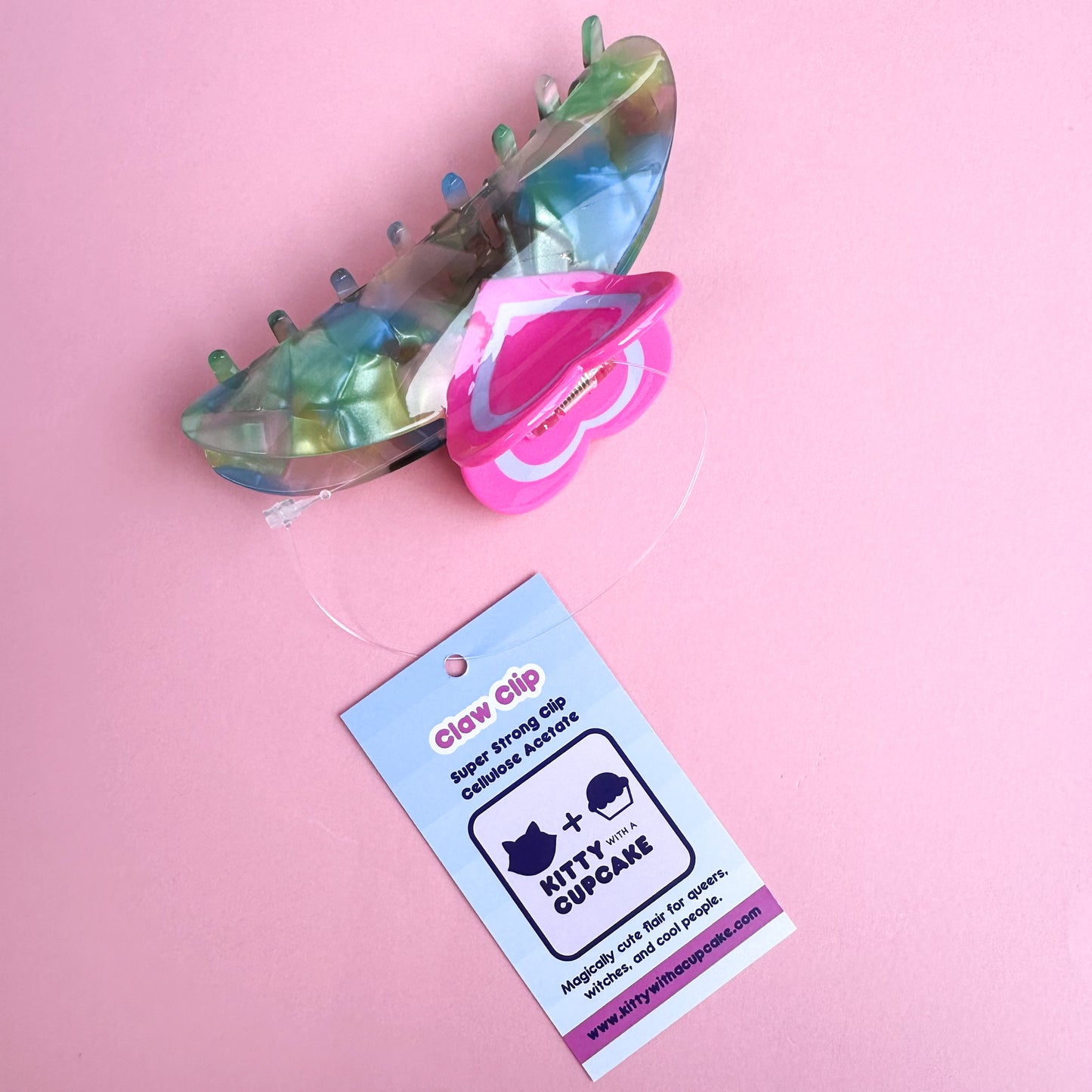 A tag attached to a claw clip with a heart handle. The tag reads "Claw Clip - Super Strong Clip Cellulose Acetate" and has the Kitty With A Cupcake Logo on it.
