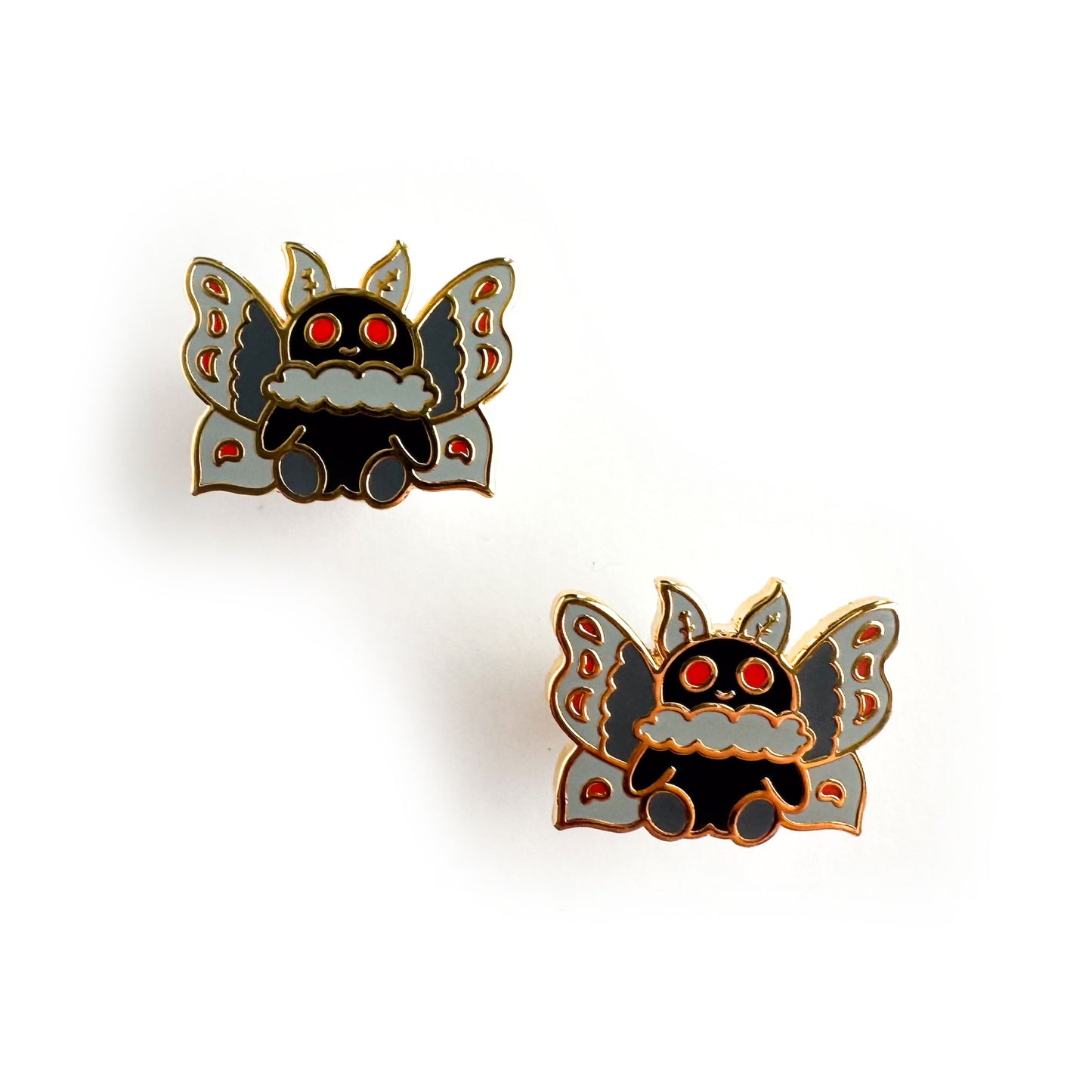 Two enamel earrings in the shape of a cute cartoon styled Mothman. They have a black body with red eyes and grey wings with red details.