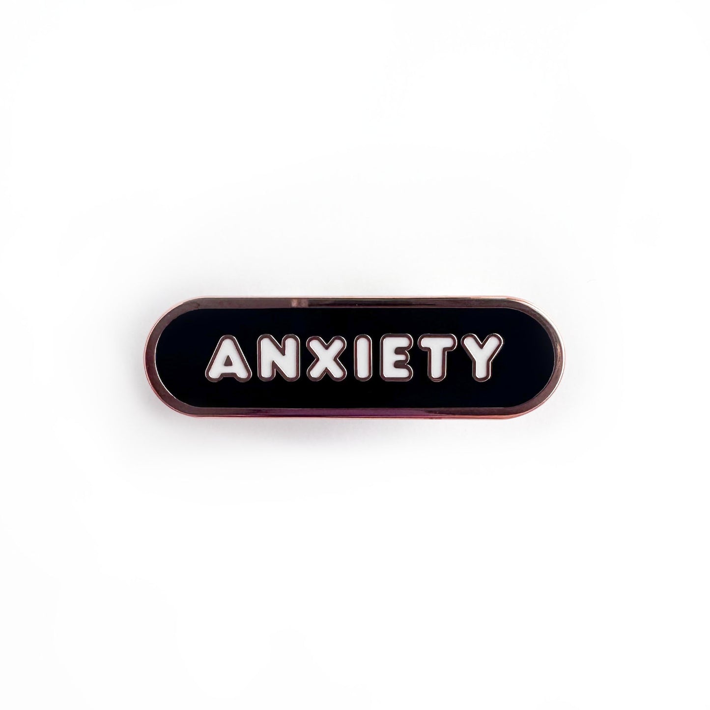Oval shaped enamel pin with "anxiety" written in white text on a black background.