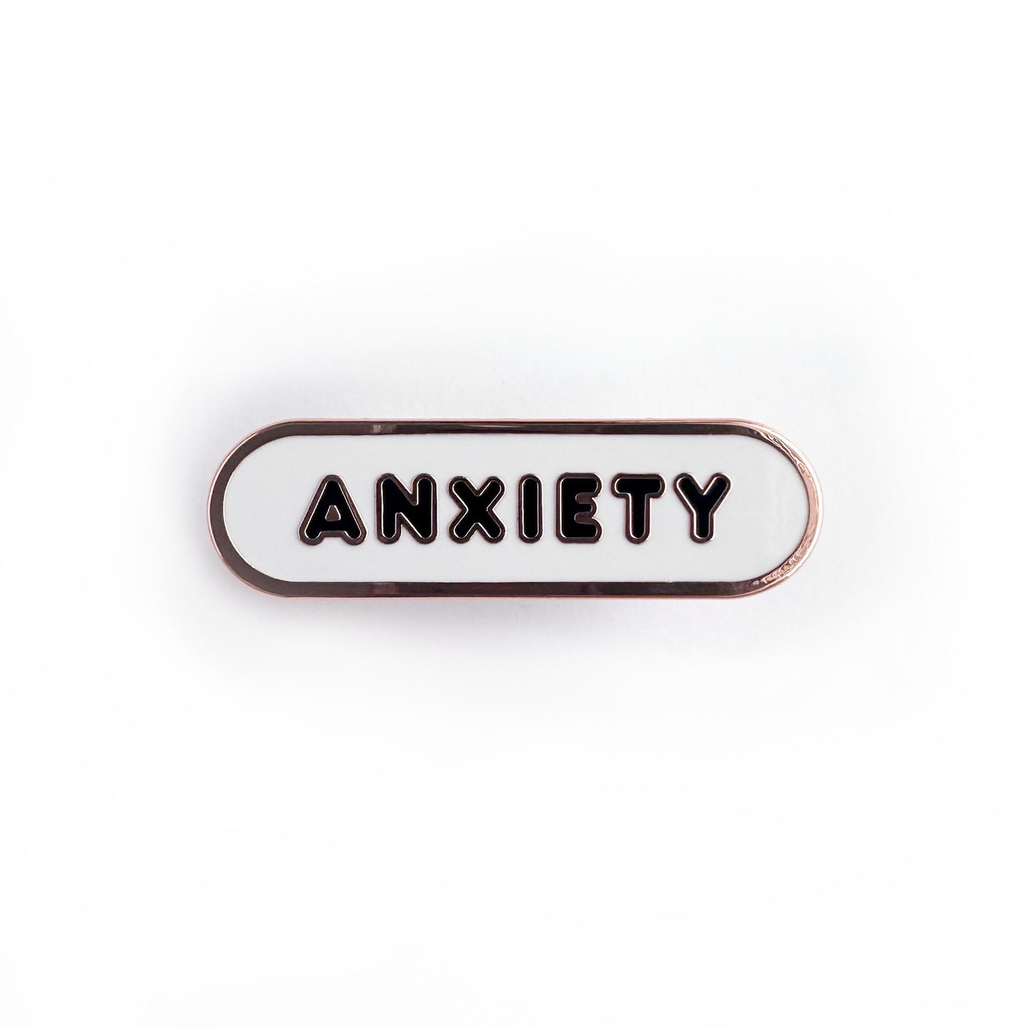 Oval shaped enamel pin with "anxiety" written in black text on a white background.