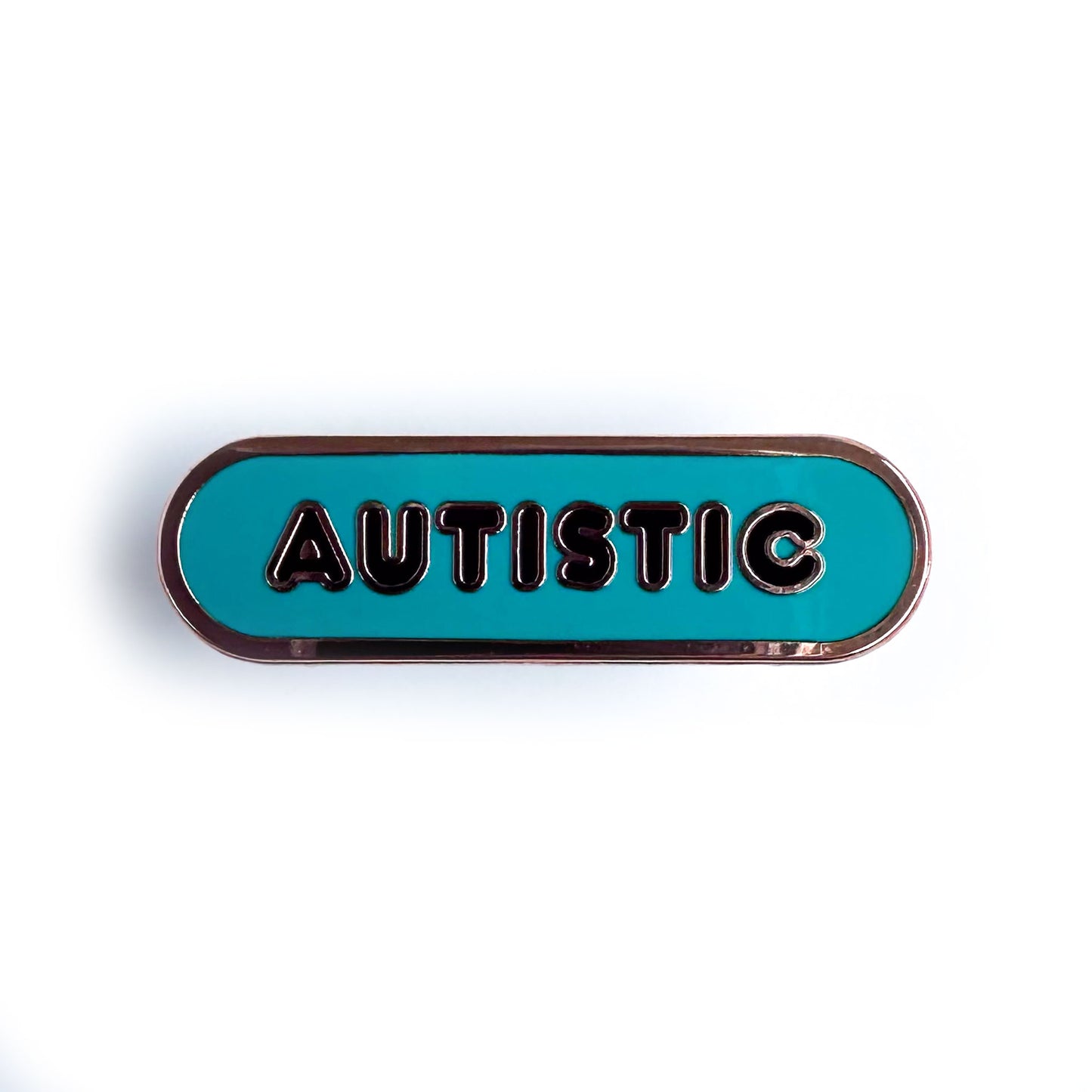 A teal oval shaped enamel pin with black bubble letters that spell "Autistic"