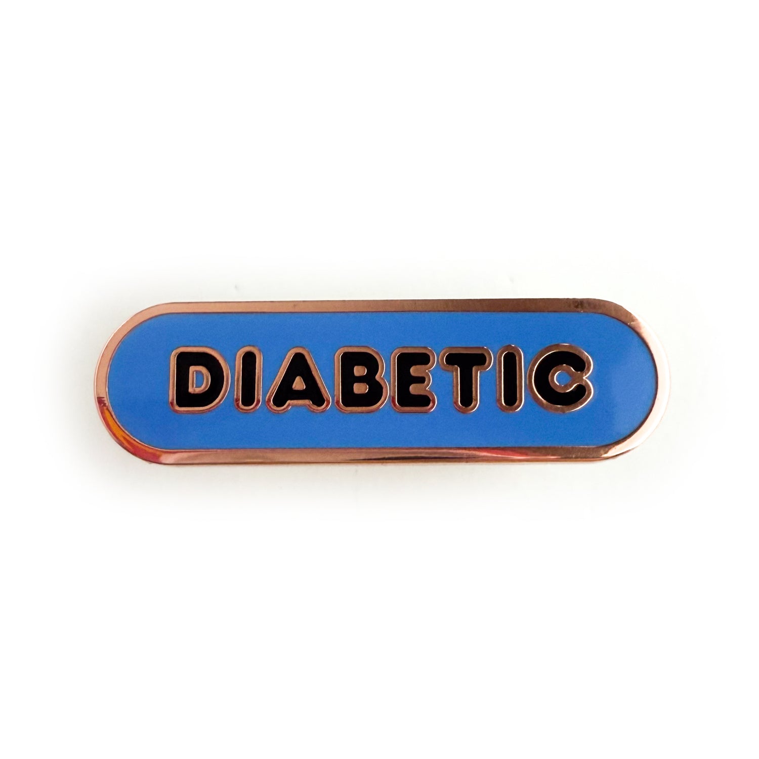 A bandaid shaped pin with the text DIABETIC in bubble letters. The background is cornflower blue and the text is black.