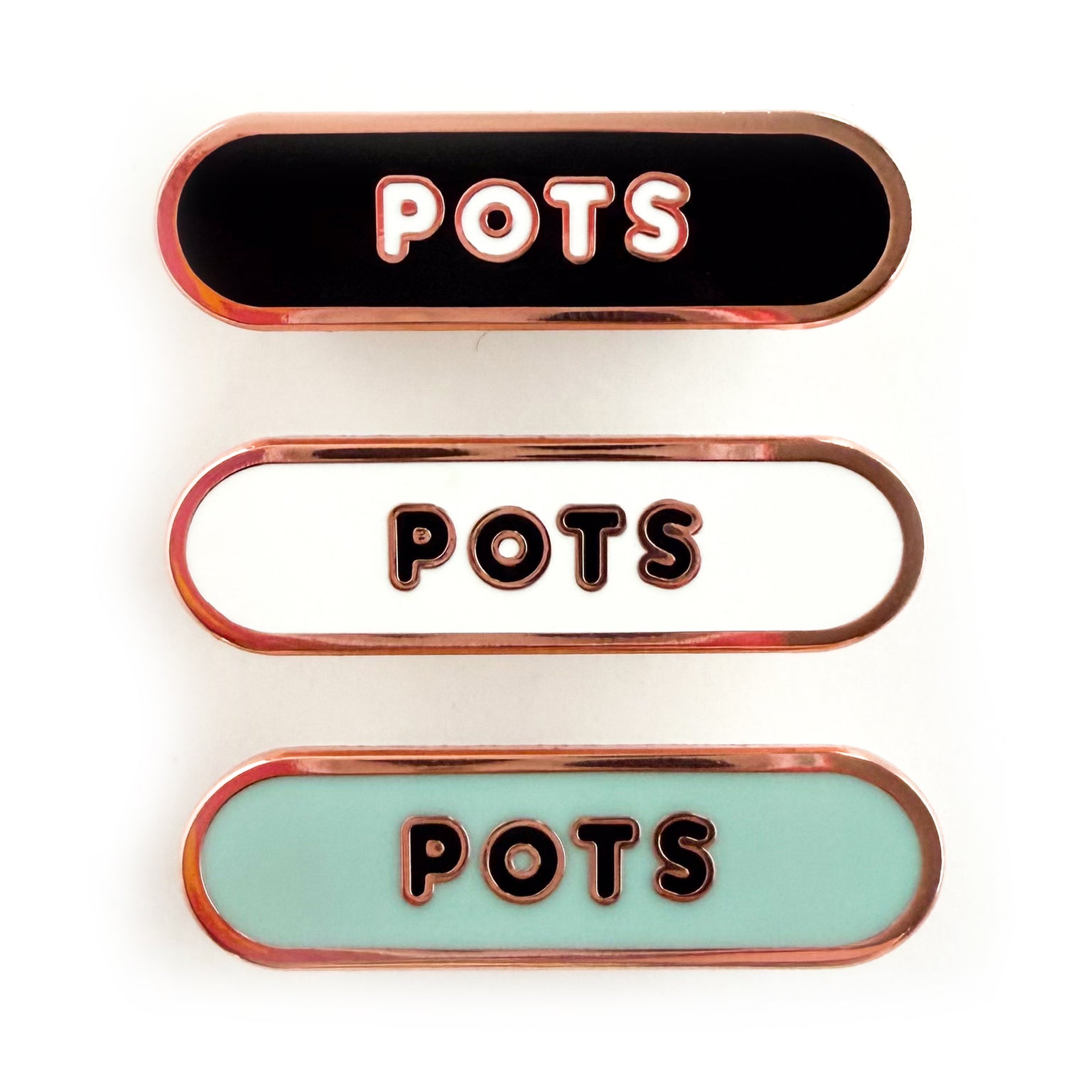 Three bandaid shaped pin with the text POTS in bubble letters. Top one black with white text, the next is white with black text, and the last is light blue with black text.