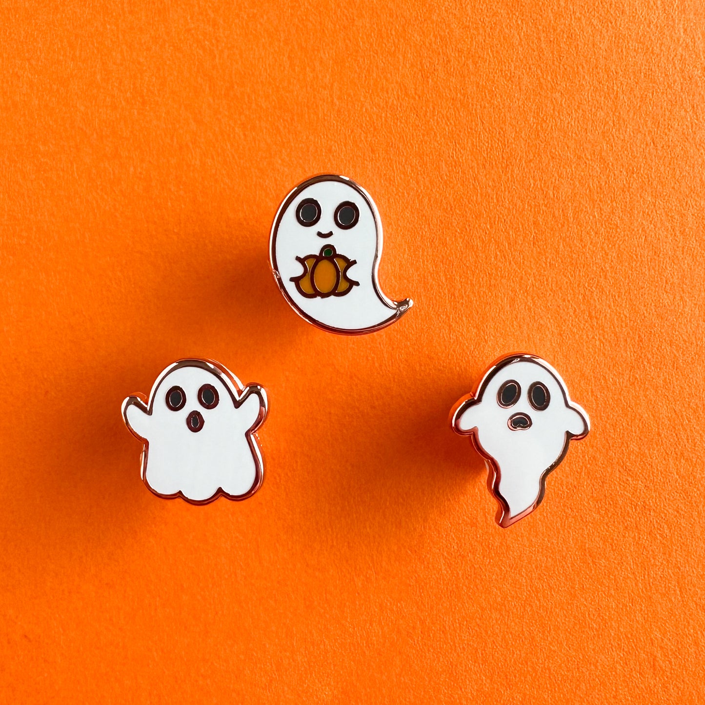 Three enamel pins with copper color metal each shaped like a cute ghost.