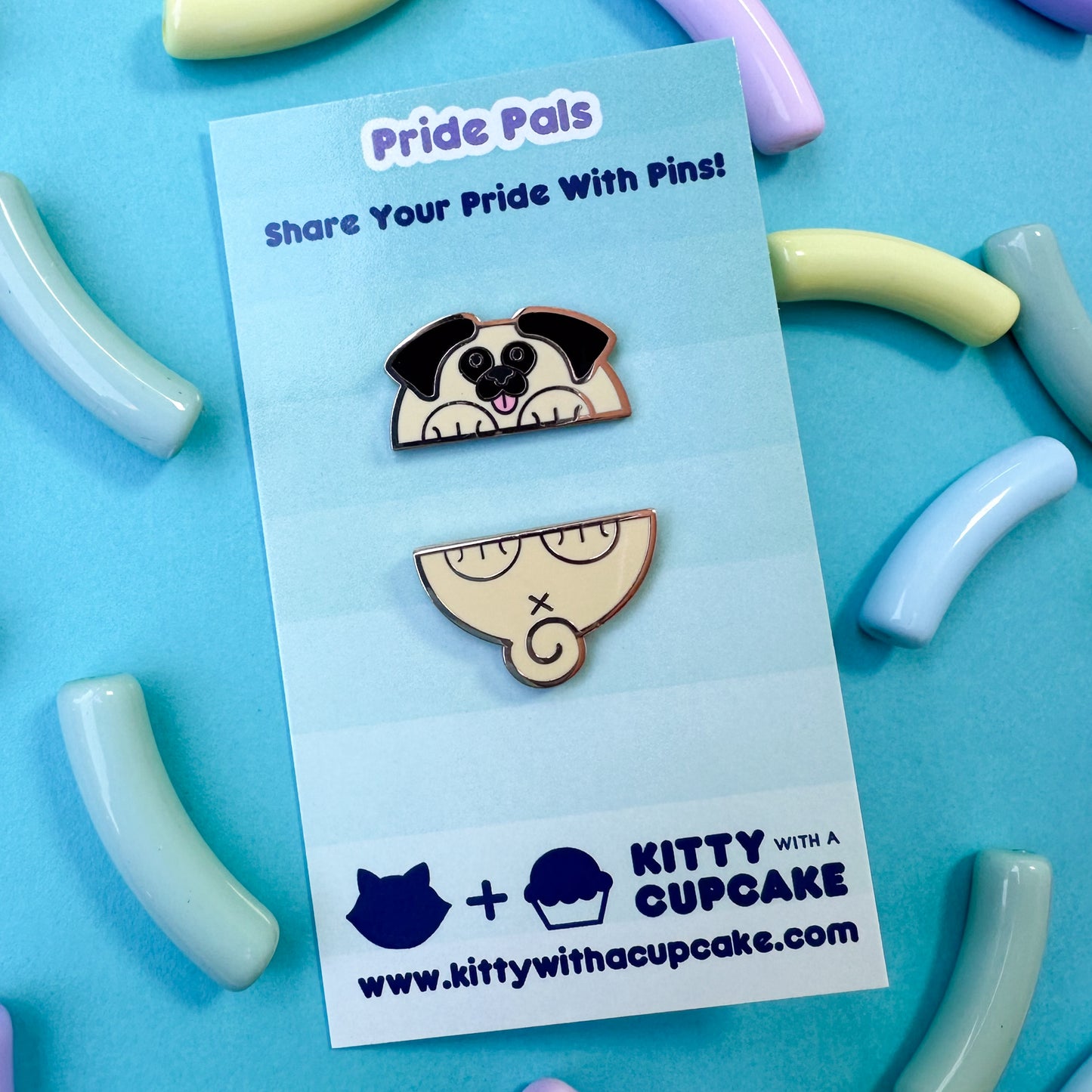 Two pins that form a cute pug illustration packaged on a card, the card is on a blue background with pastel beads around it.