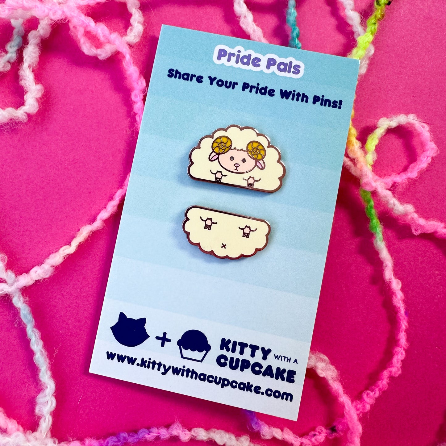 Two cute enamel pins that come together to form a sheep packaged on a blue card on top of a hot pink background with boucle yarn around it.