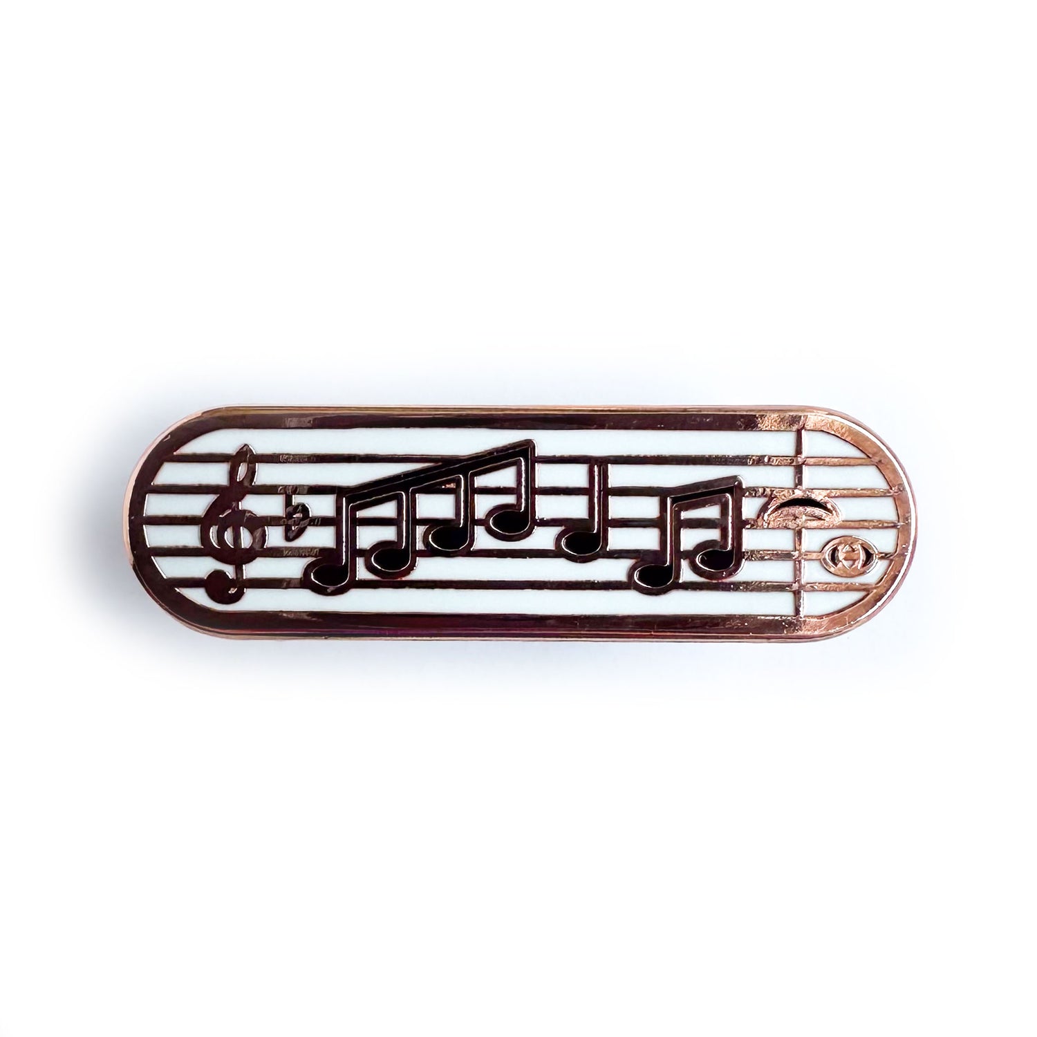 A capsule shaped enamel pin with a music staff with a treble clef and music notes on it.