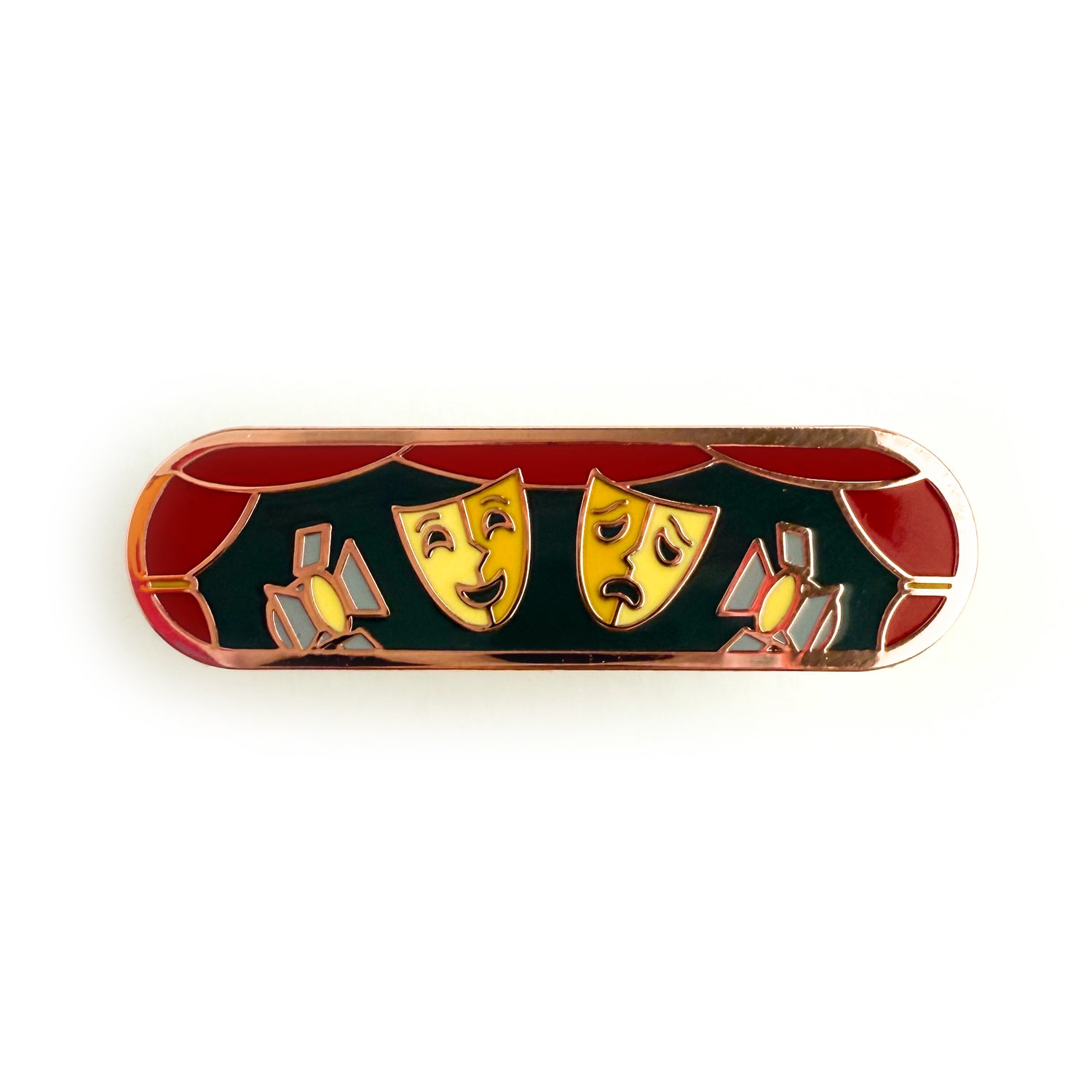 A bandaid shaped enamel pin with theater themed illustrations. There is a red curtain boarder around both a comedy and tragedy mask and two stage lights.