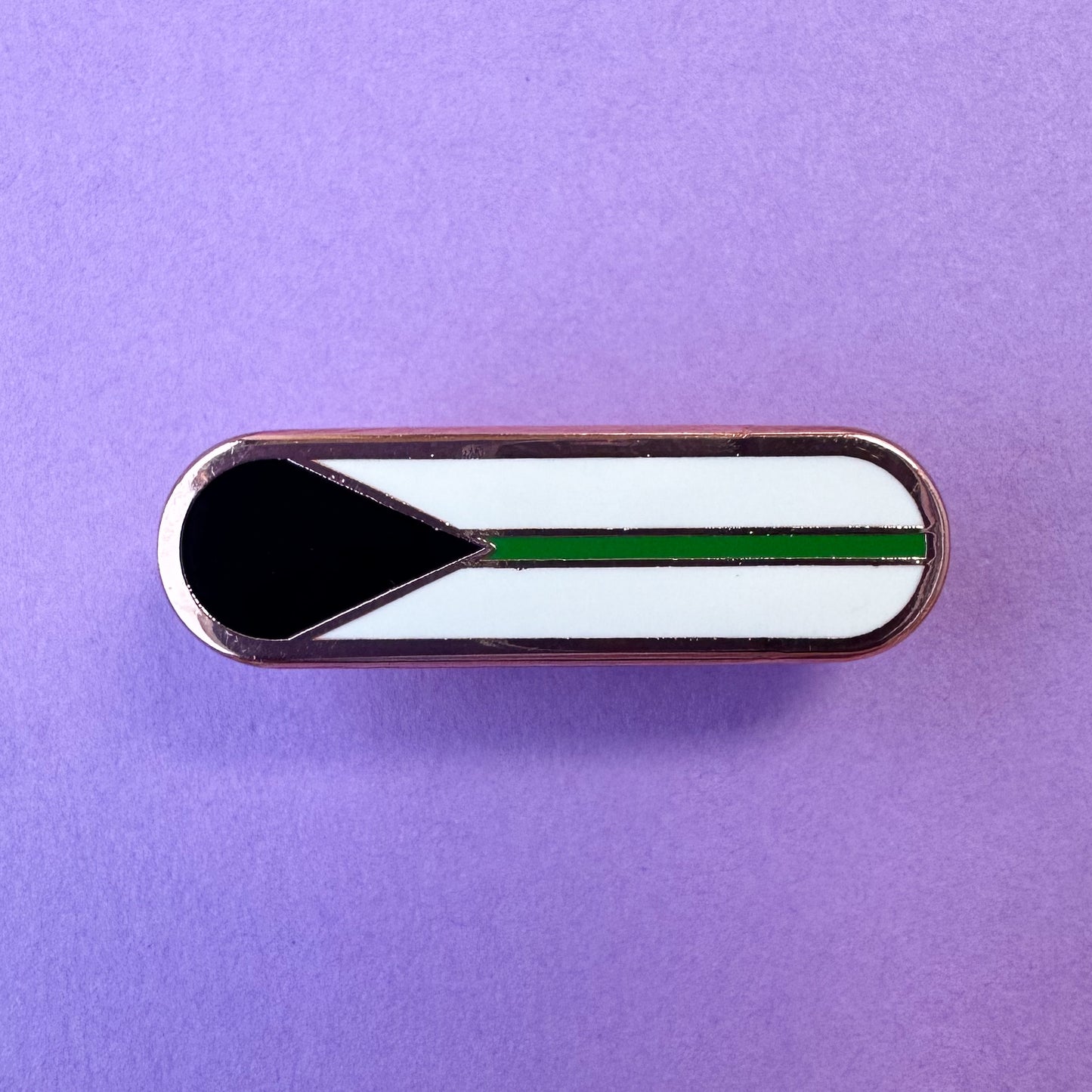 A bandaid shaped pin with the imagery of the Demiromantic pride flag on it, a black triangle an da green stripe on a white background. The pin is on a lavender background.