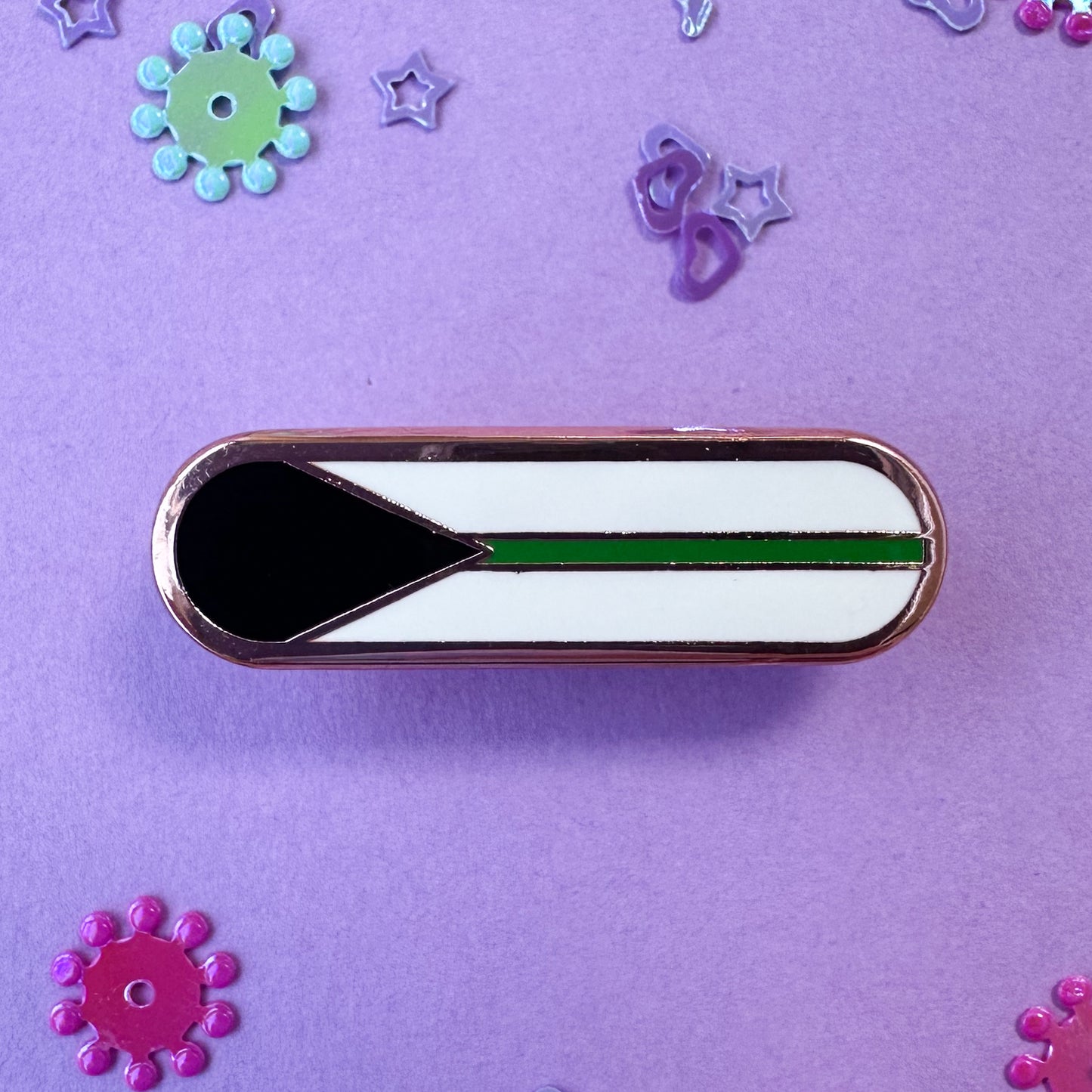 A bandaid shaped pin with the imagery of the Demiromantic pride flag on it, a black triangle an da green stripe on a white background. The pin is on a lavender background with glitter around it.