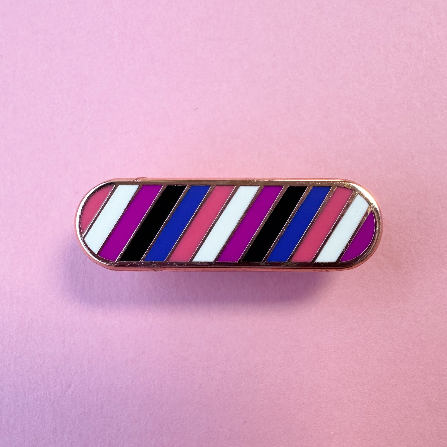 A capsule shaped pin in the colors of the Gender Fluid pride flag on a pink background.
