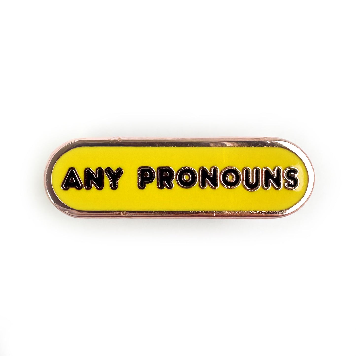 A bandaid shaped pin that is yellow with black words on it that read "Any Pronouns"