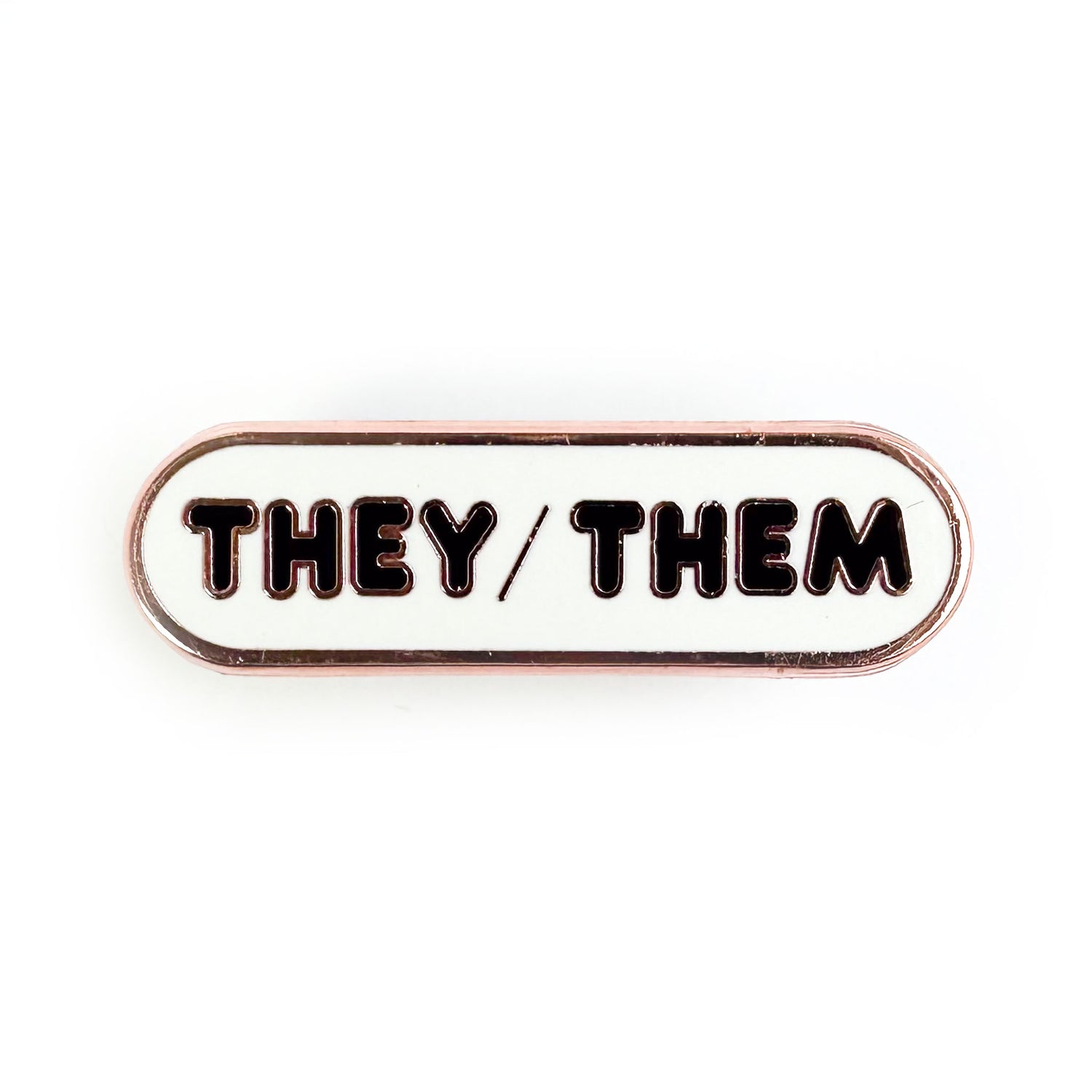 An oval shaped pin with a white background and black bubble letters on it, the letters spell "They/Them" on it.