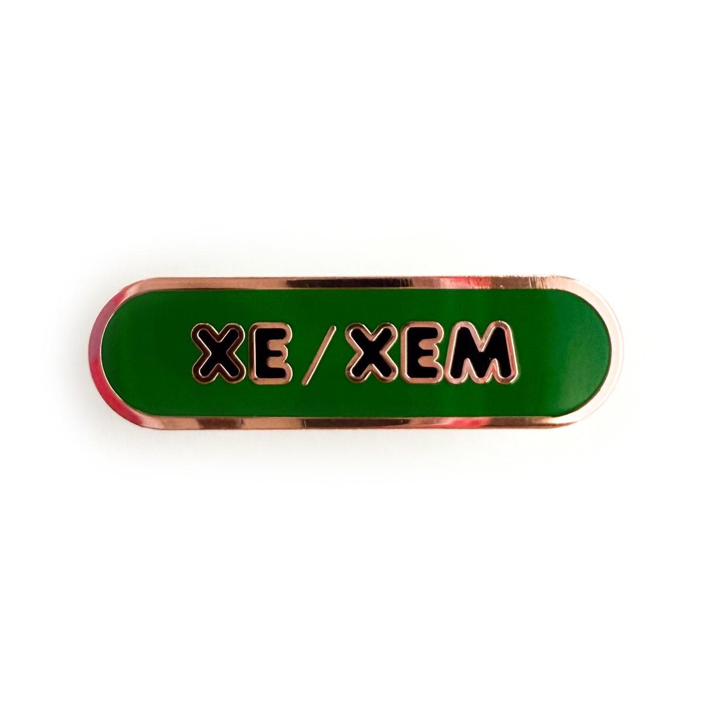 A bandaid shaped pin with the text XE/XEM in bubble letters. The background is green and the text is black.