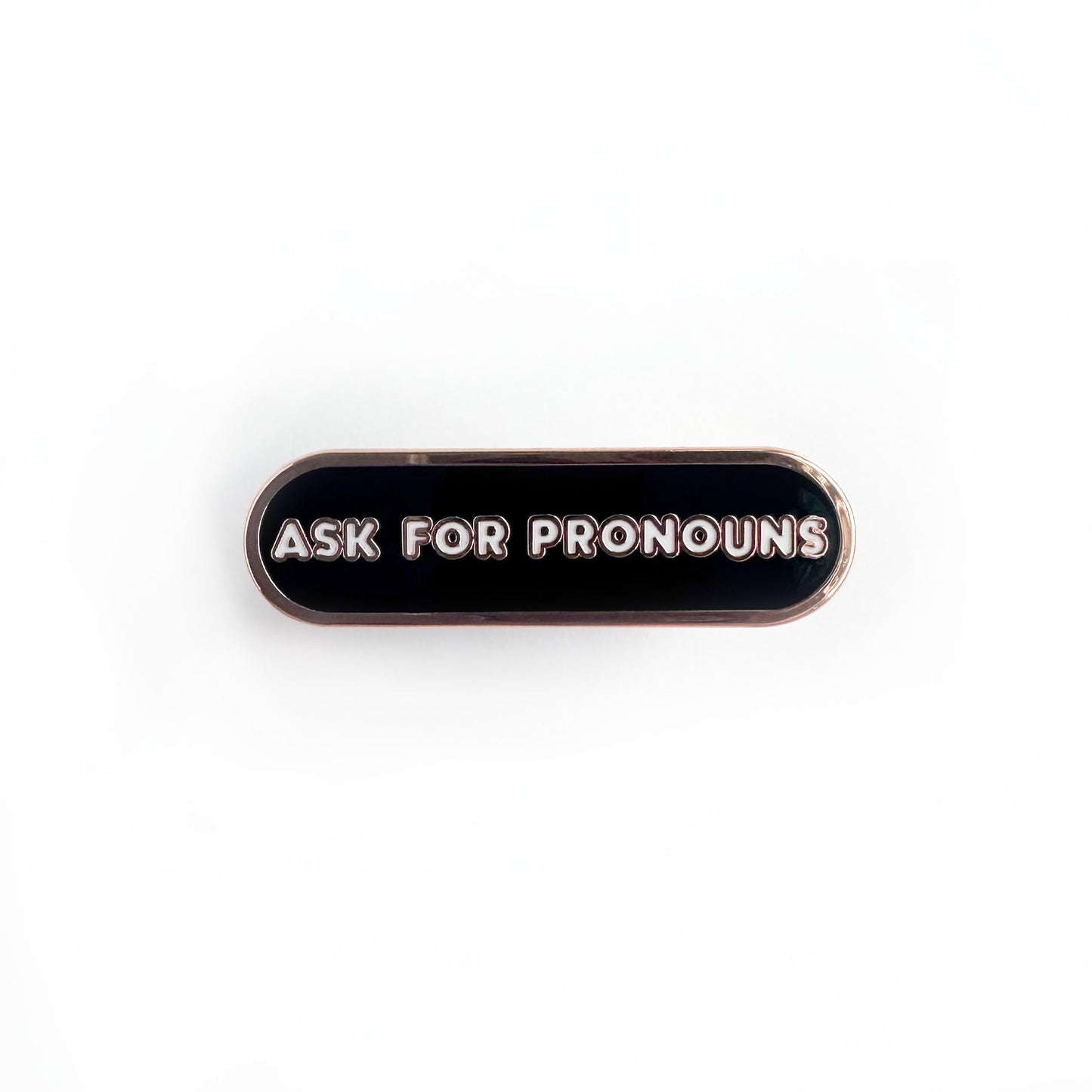 Oval shaped enamel pin with "ask for pronouns" written in white text on a black background.