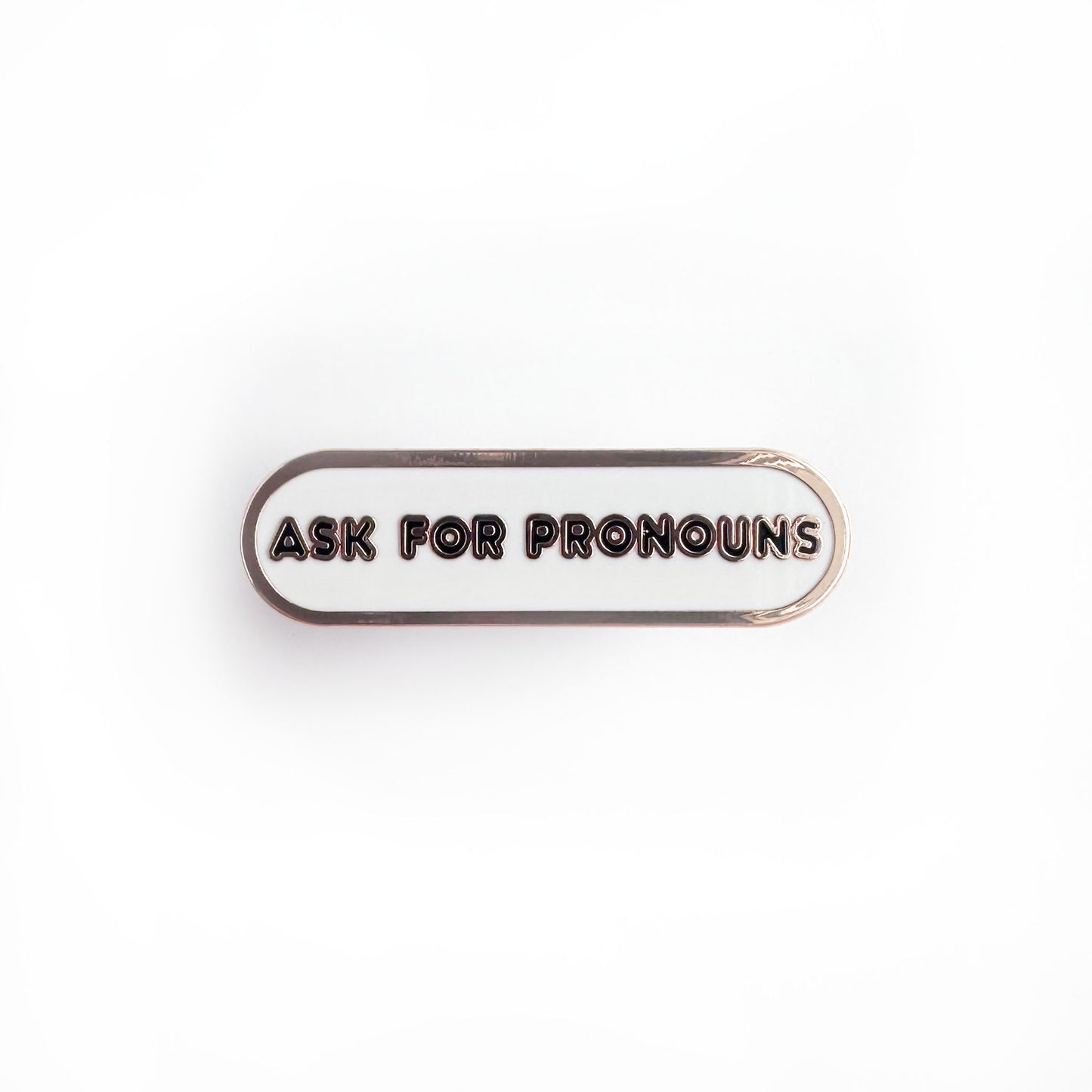 Oval shaped enamel pin with "ask for pronouns" written in black text on a white background.