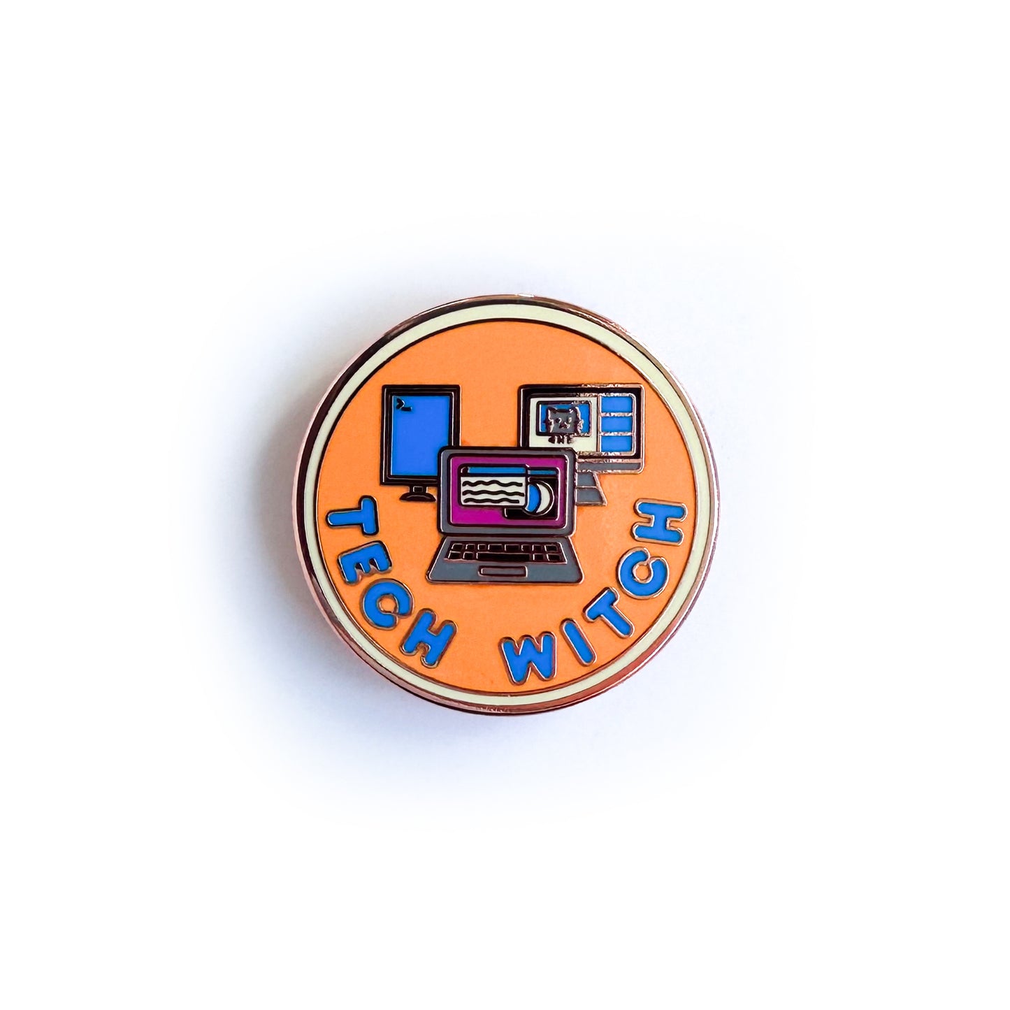 A circular merit badge style pin with the words "Tech Witch" on it. There are images of a laptop surrounded by two computer monitors on it. The pin is orange with a yellow border and blue words.
