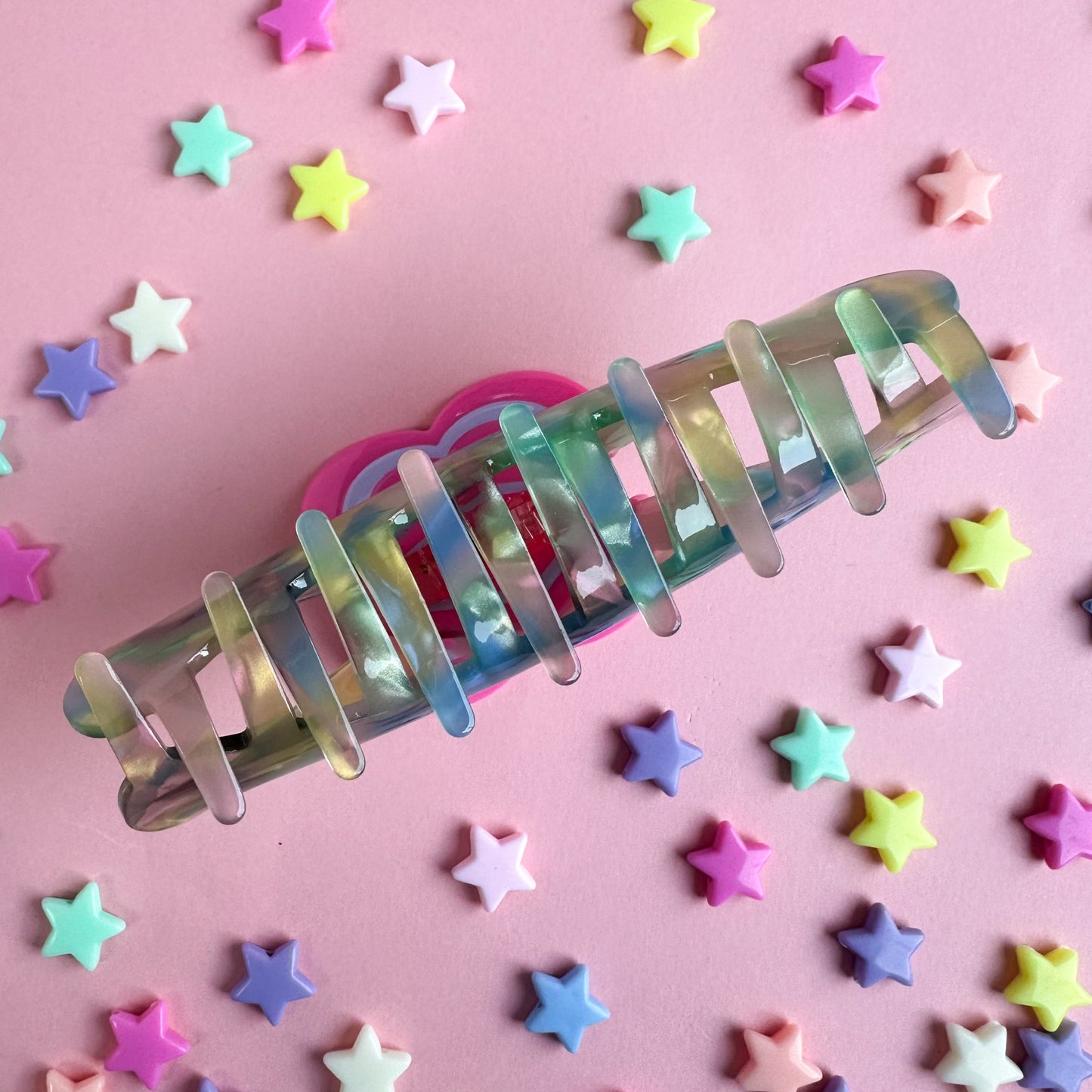 The teeth of a large claw clip made out of pastel pearly acetate. The clip is on a pink background with star beads around it.