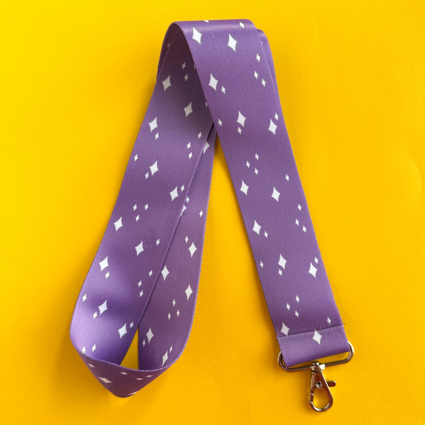 A purple lanyard with white sparkle illustrations on it, the lanyard is folded in half.