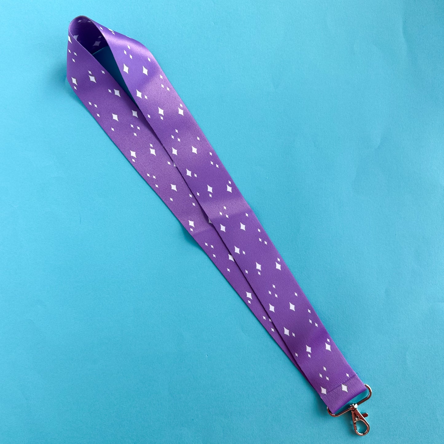 A long purple lanyard with sparkle illustrations on it. The lanyard is on a blue paper background.
