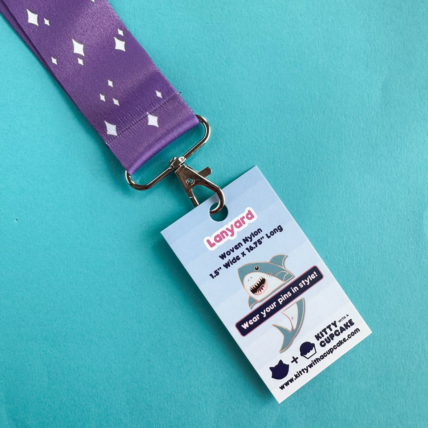 The clip of a purple lanyard with a card in the clip that reads "Lanyard Woven Nylon - Wear your pins in style" The card has a cartoon of a shark on it.