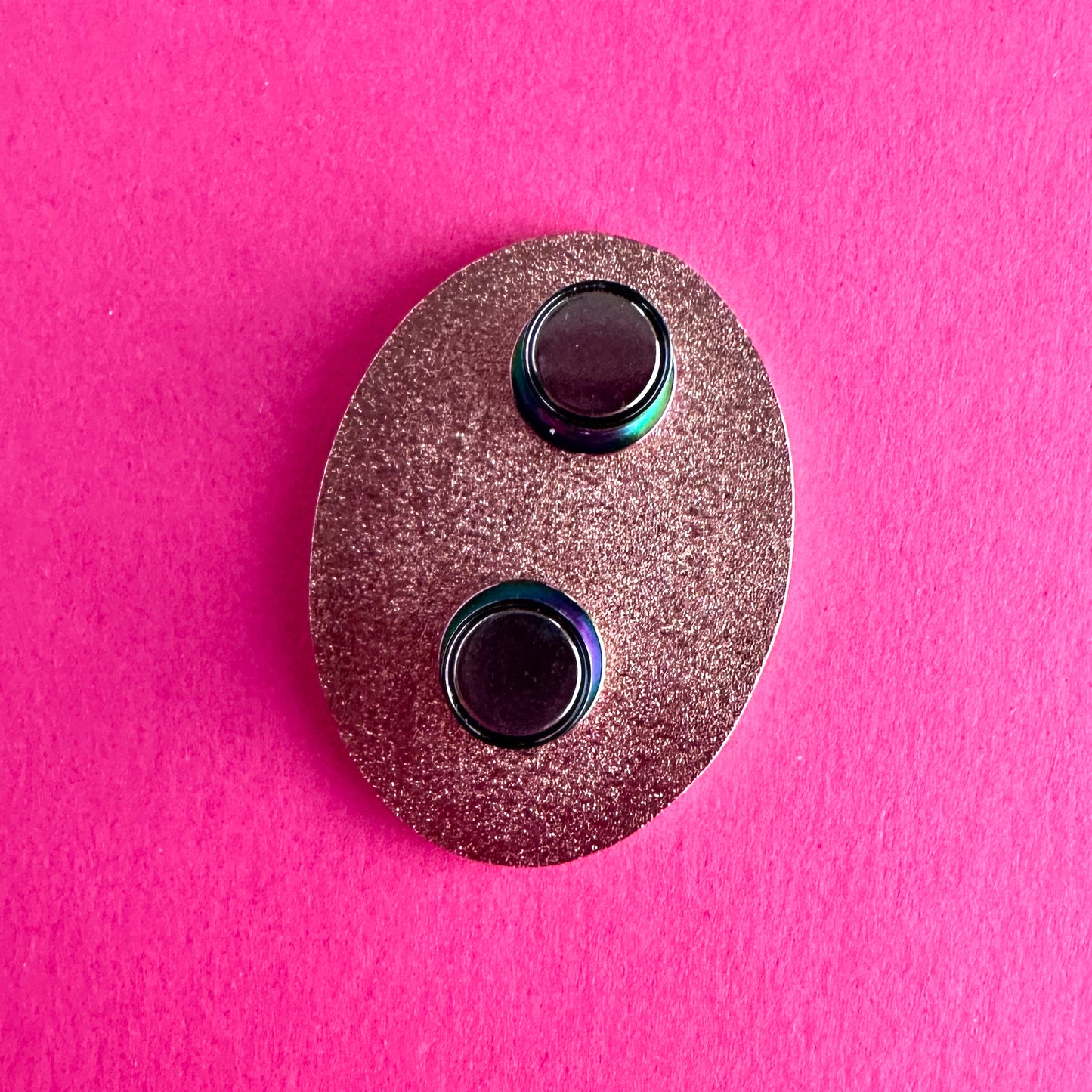An enamel pin face down with two magnetic pin backs on its pin posts.