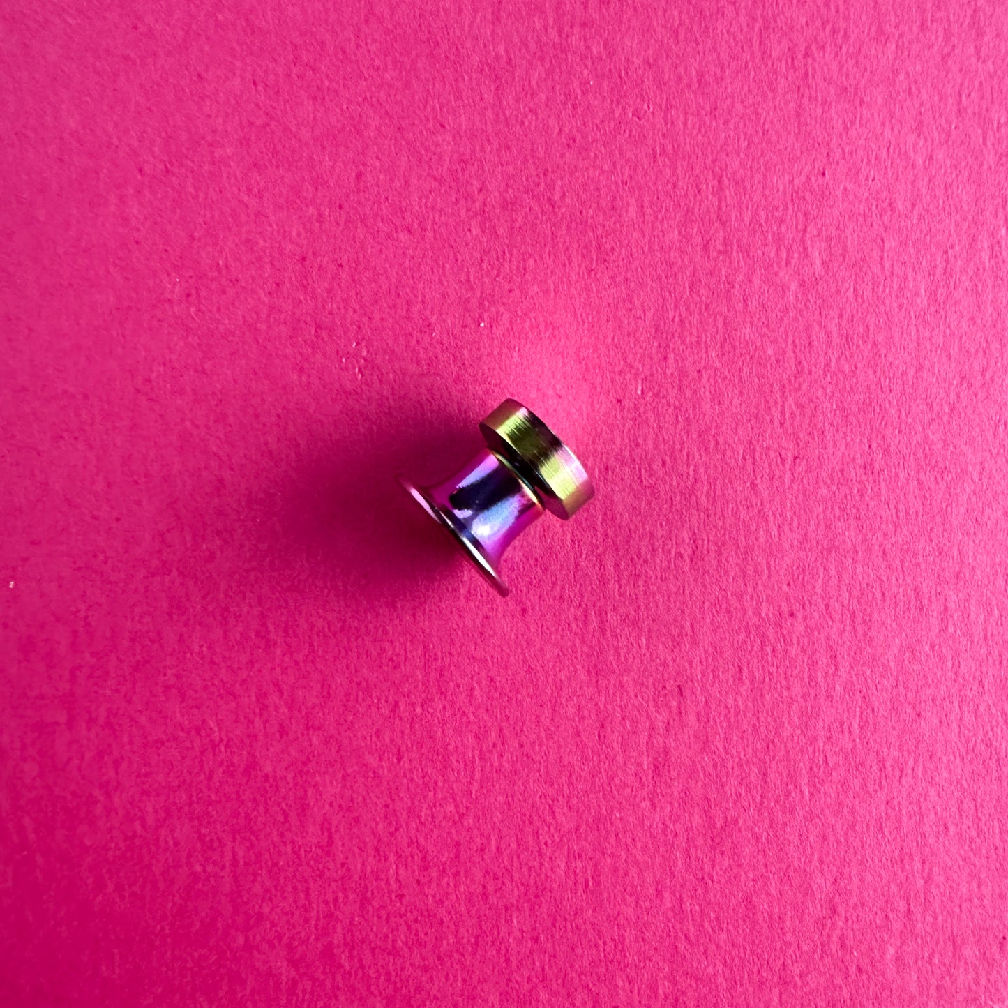 A rainbow magnetic pin back on a pink paper background.