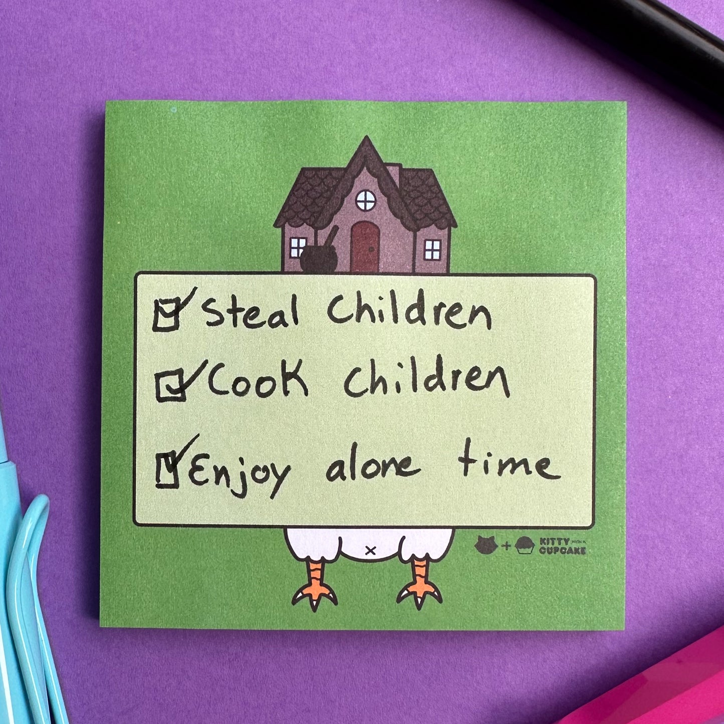 A square pad of green sticky notes featuring an illustration of Baba Yaga's house on a purple background with pens surrounding the pad. There is a to-do list written on the pad that reads "Steal Children, Cook Children, Enjoy alone time" all of these items are checked off.