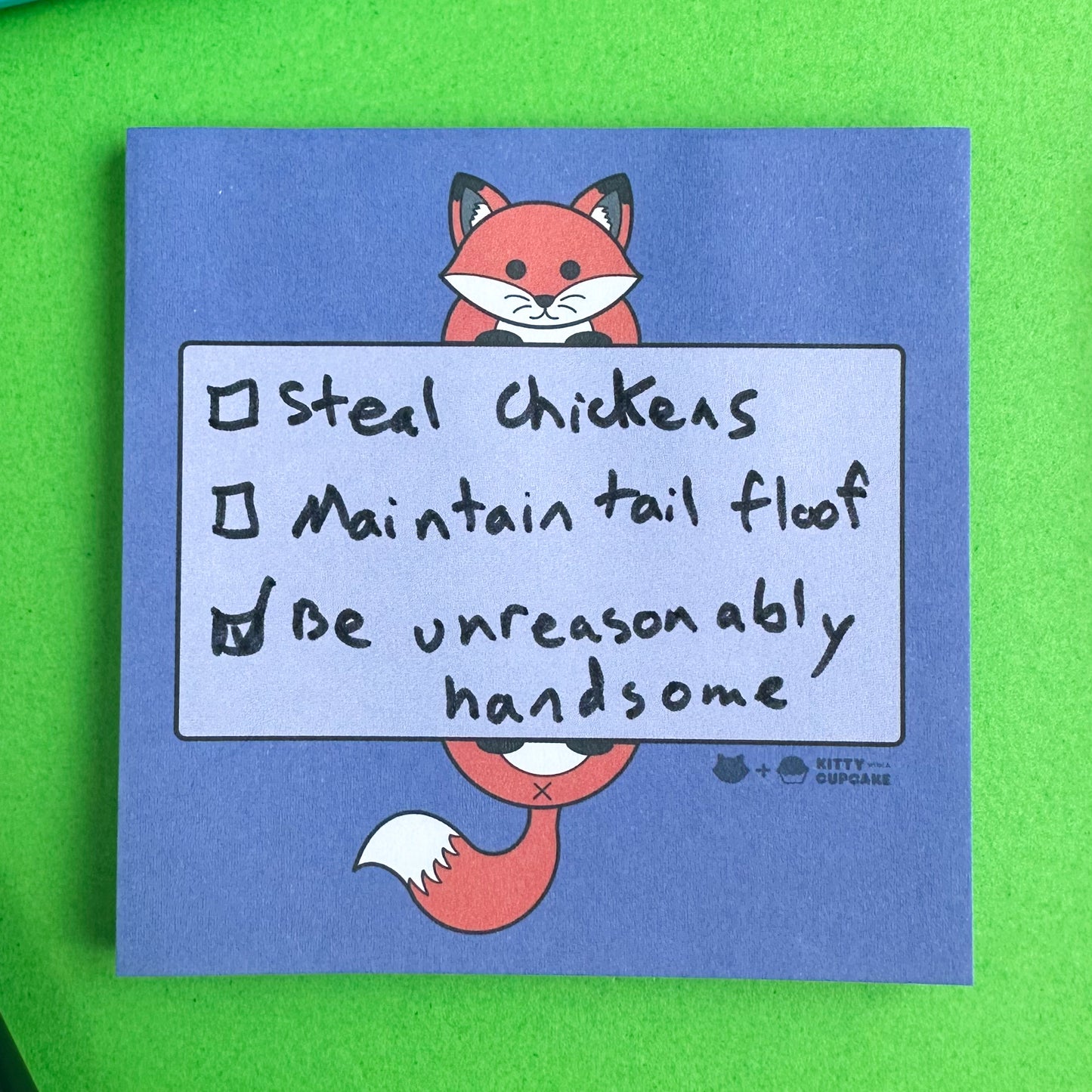 A pad of purple sticky notes with an illustration of a fox holding a box that is meant to be the area to write in. There is a handwritten checklist that reads "Steal Chickens, Maintain tail floor, Be unreasonably handsome" on it.