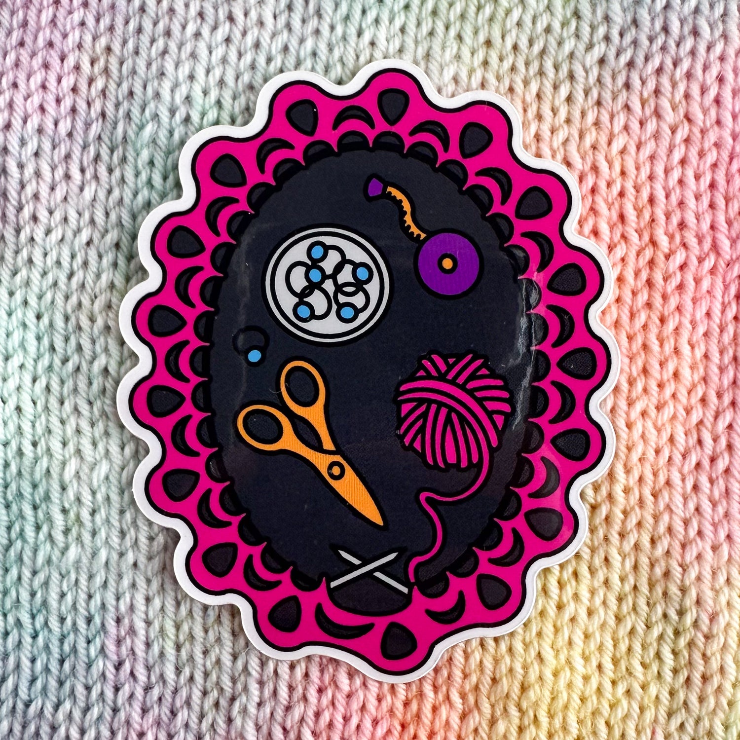 A vinyl sticker with an illustration of a in progress knitting project made from pink yarn. There are illustrations of knitting tools inside the project too including scissors, stitch markers and a tape measure. The sticker is sitting on a background of stockinette stitch in pastel colors.