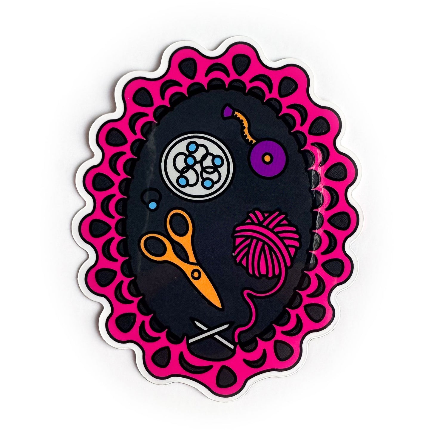 A vinyl sticker depicting a knitting project still on the needles with knitting tools inside of it including scissors, stitch markers, a pink yarn ball and a tape measure.
