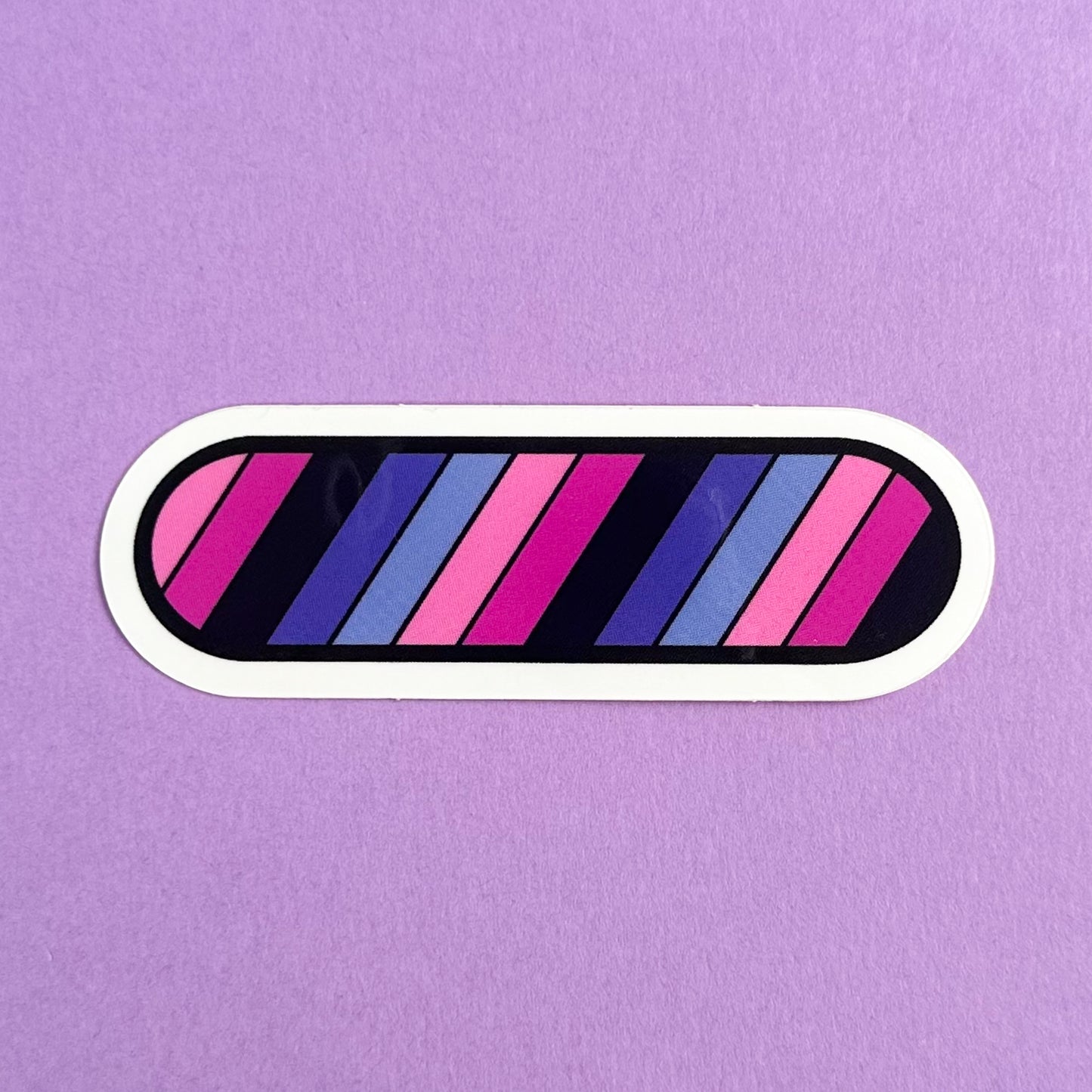 A vinyl sticker in the shape of an oval with diagonal stripes of the Omni Pride Flag. The stick is on a purple background.