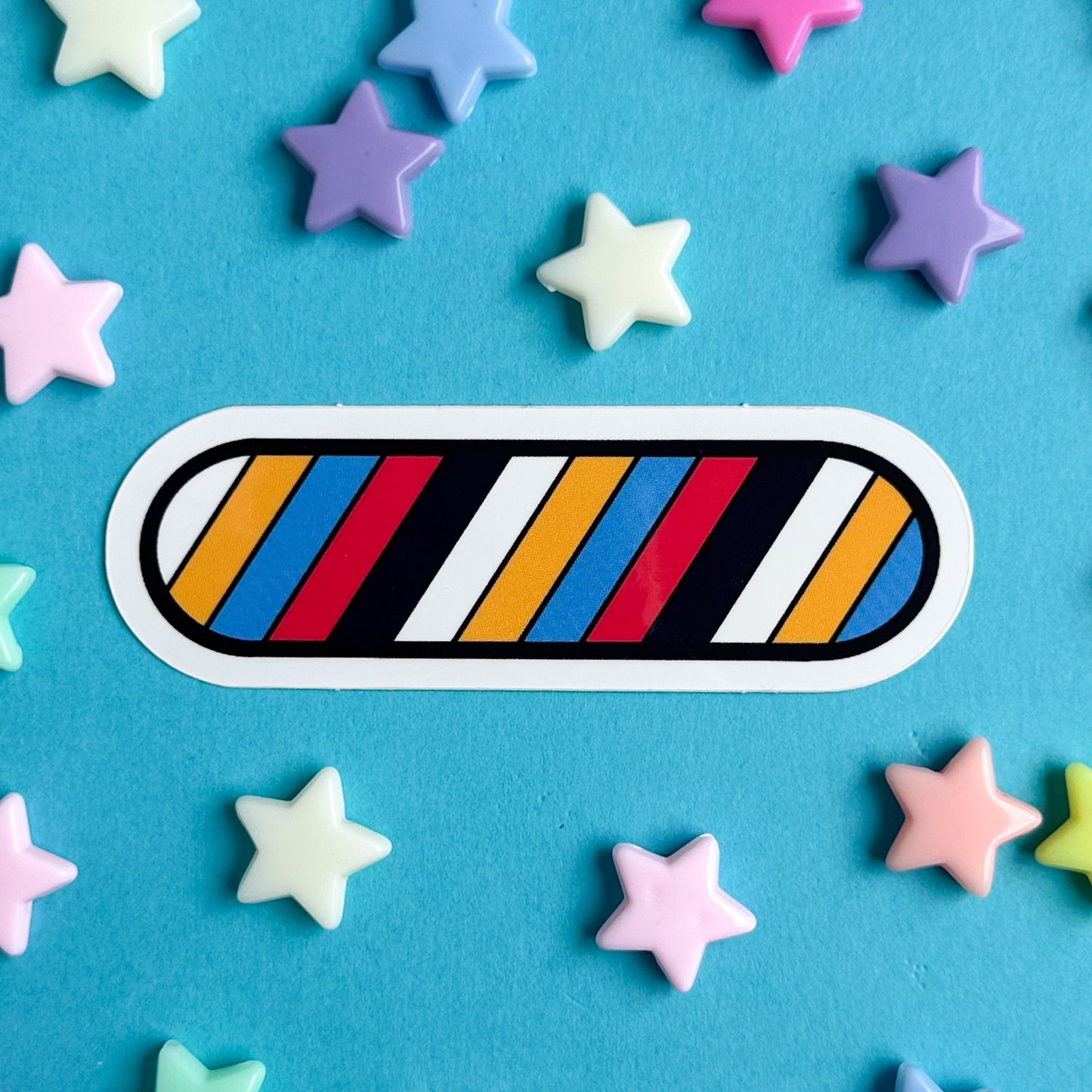 A capsule shaped vinyl sticker with diagonal stripes of the Poly Pride Flag on a blue background with pastel star beads around it.