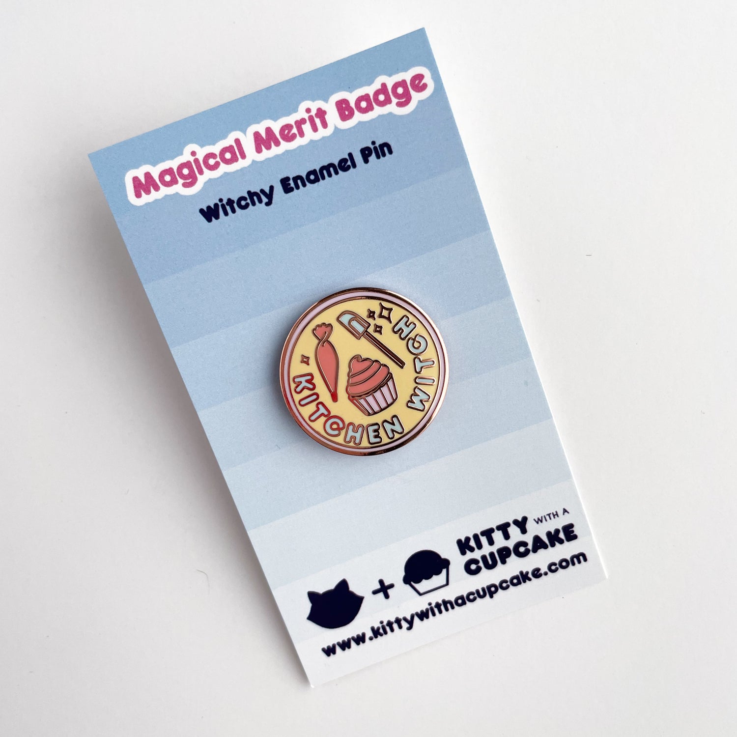A circular Kitchen Witch pin on a card with blue to white gradient background that reads "Magical Merit Badge" and "Witchy Enamel Pin" across the top.