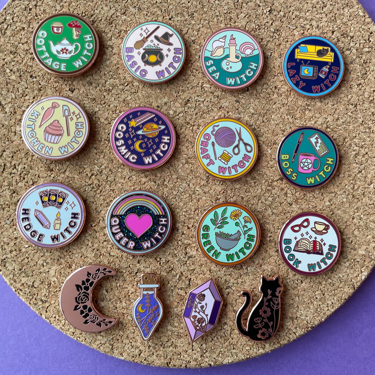 A collection of pins on a circular cork board on top of a purple background. 12 of the pins are circles in the style of merit badges. The badges are for different types of witches such as Basic Witch, Hedge Witch, Green Witch, Craft Witch, etc. Under these are pins shaped like a crescent moon, a potion bottle, a crystal and a cat.