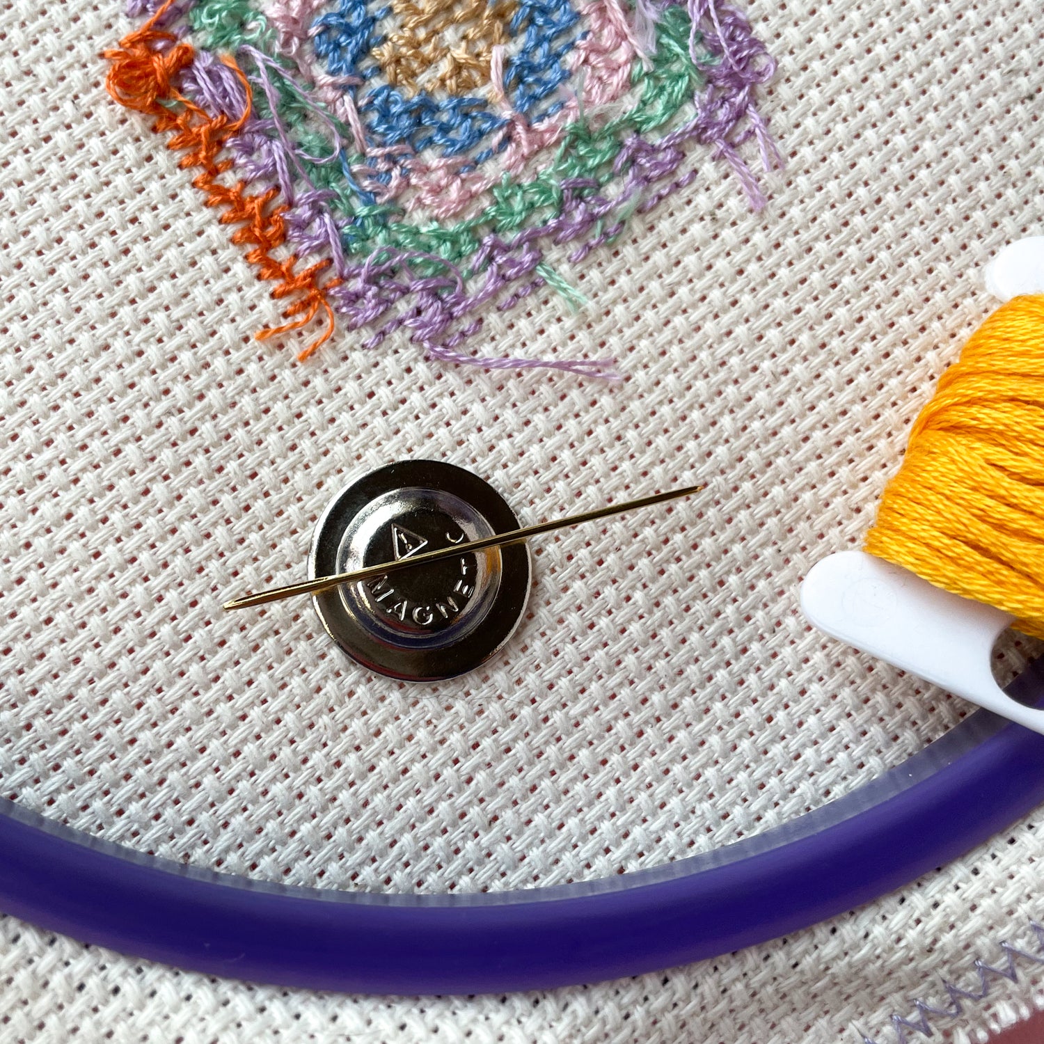 The magnetic back of a needle minder holding a needle and displayed on an embroidery hoop