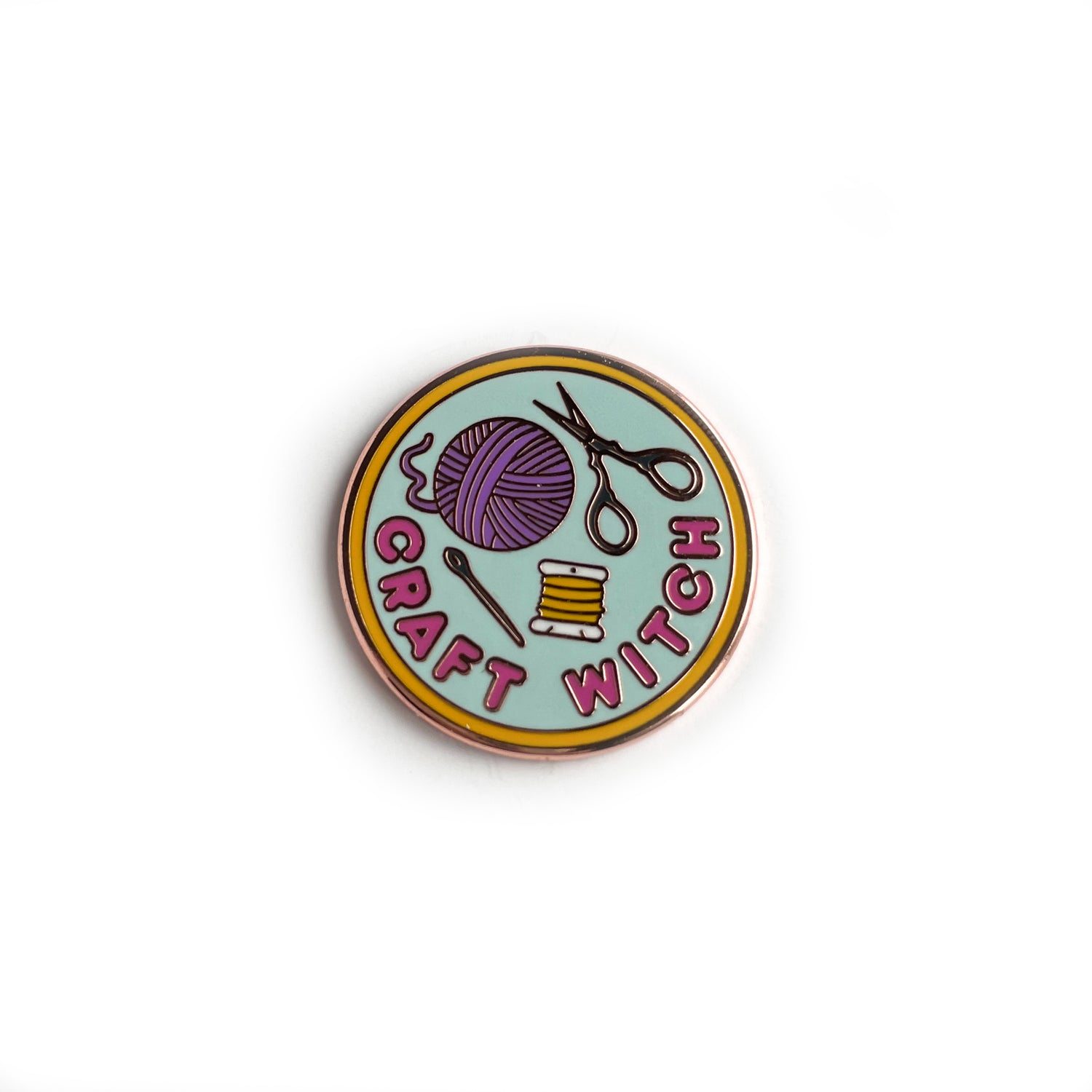 An enamel needle minder shaped like a circle with the words "Craft Witch" and a yarn ball and scissors on it.