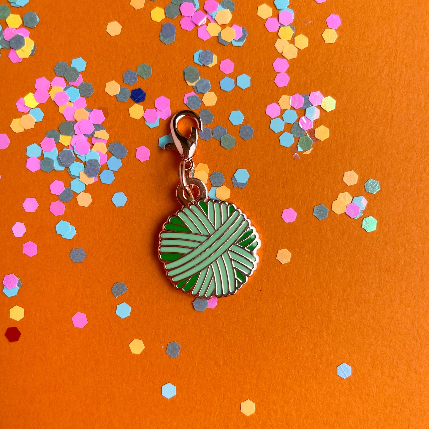 A mint green yarn ball charm on an orange background covered in confetti