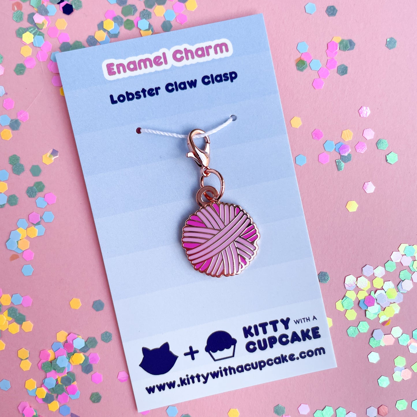 A pink yarn ball shaped charm on a blue background. 