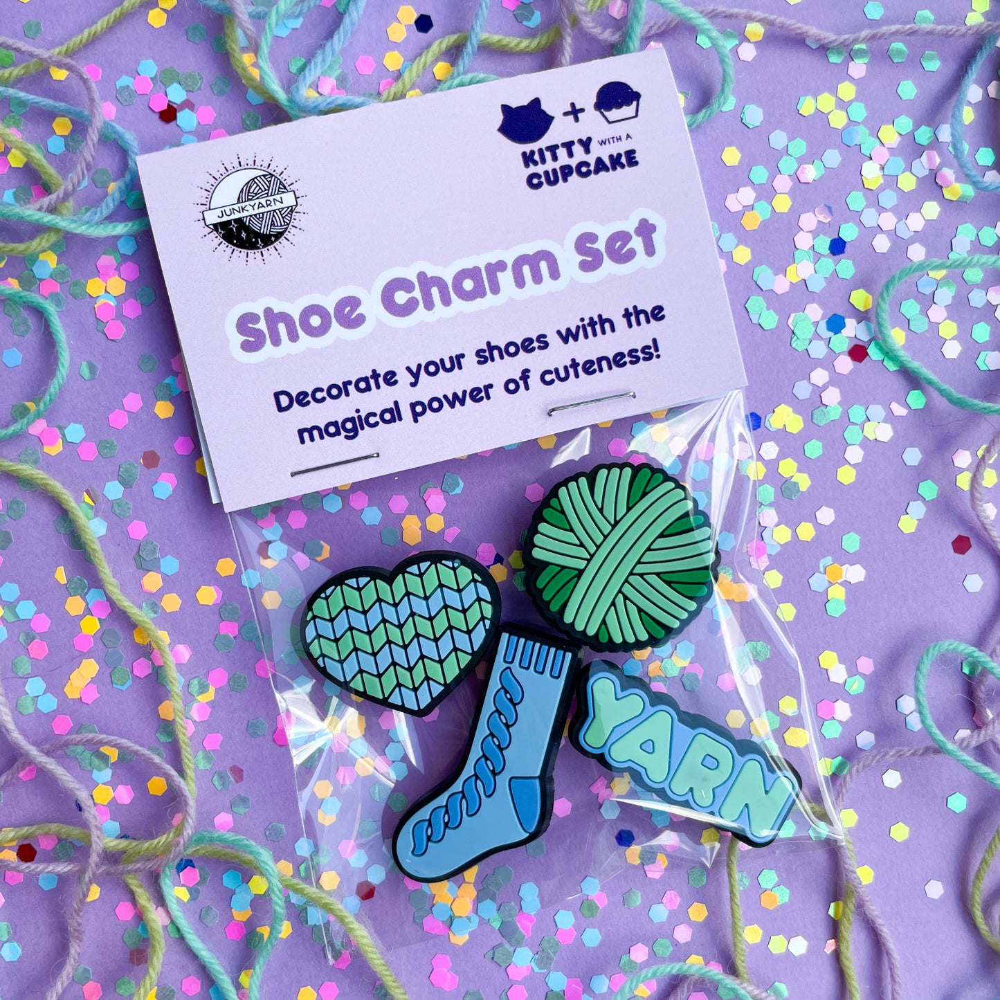 A header card with a plastic bag with charms shaped like a heart, yarn ball, sock and the word yarn in it. The header card is pink and reads "shoe charm set".