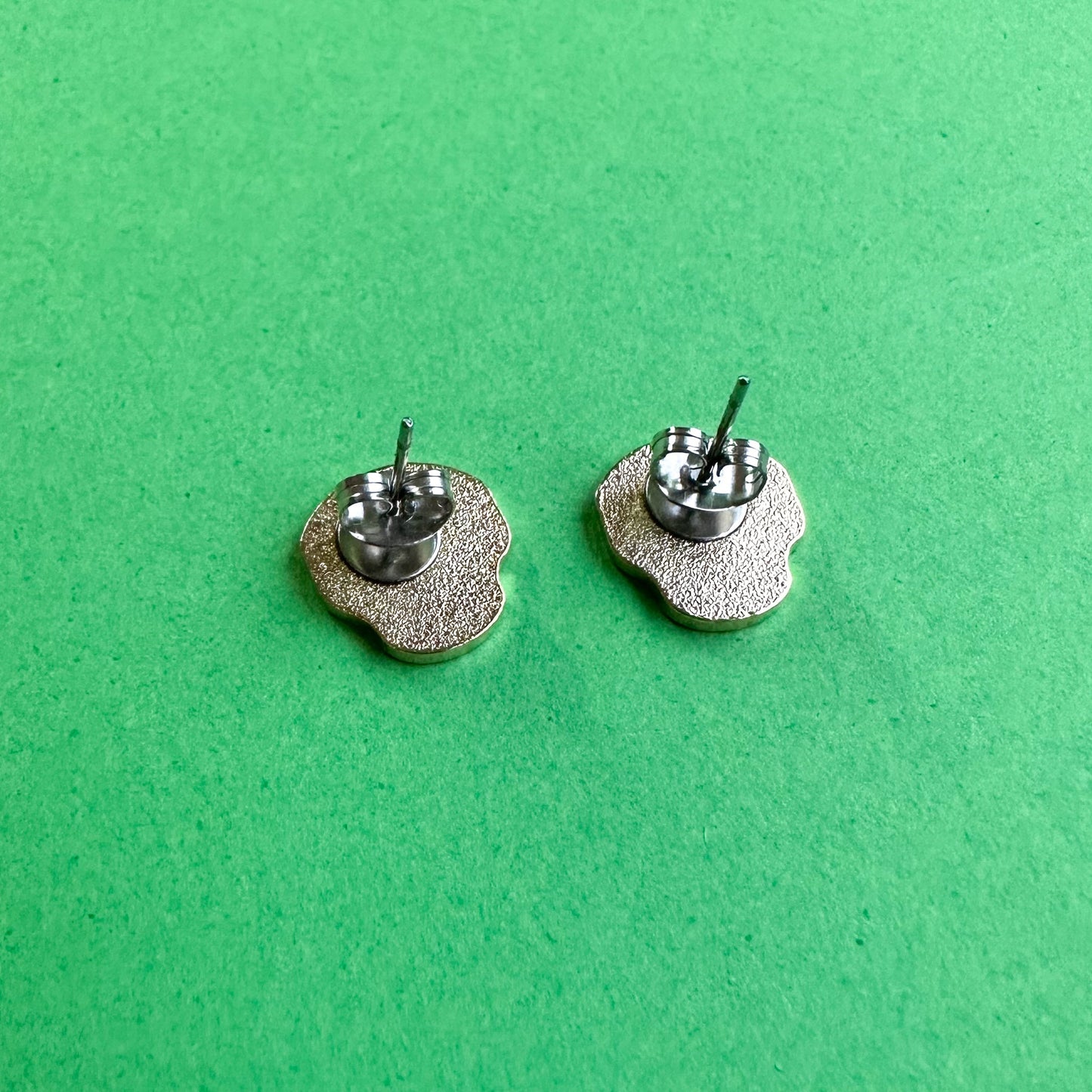 The back of a set of skull shaped earrings on a green background