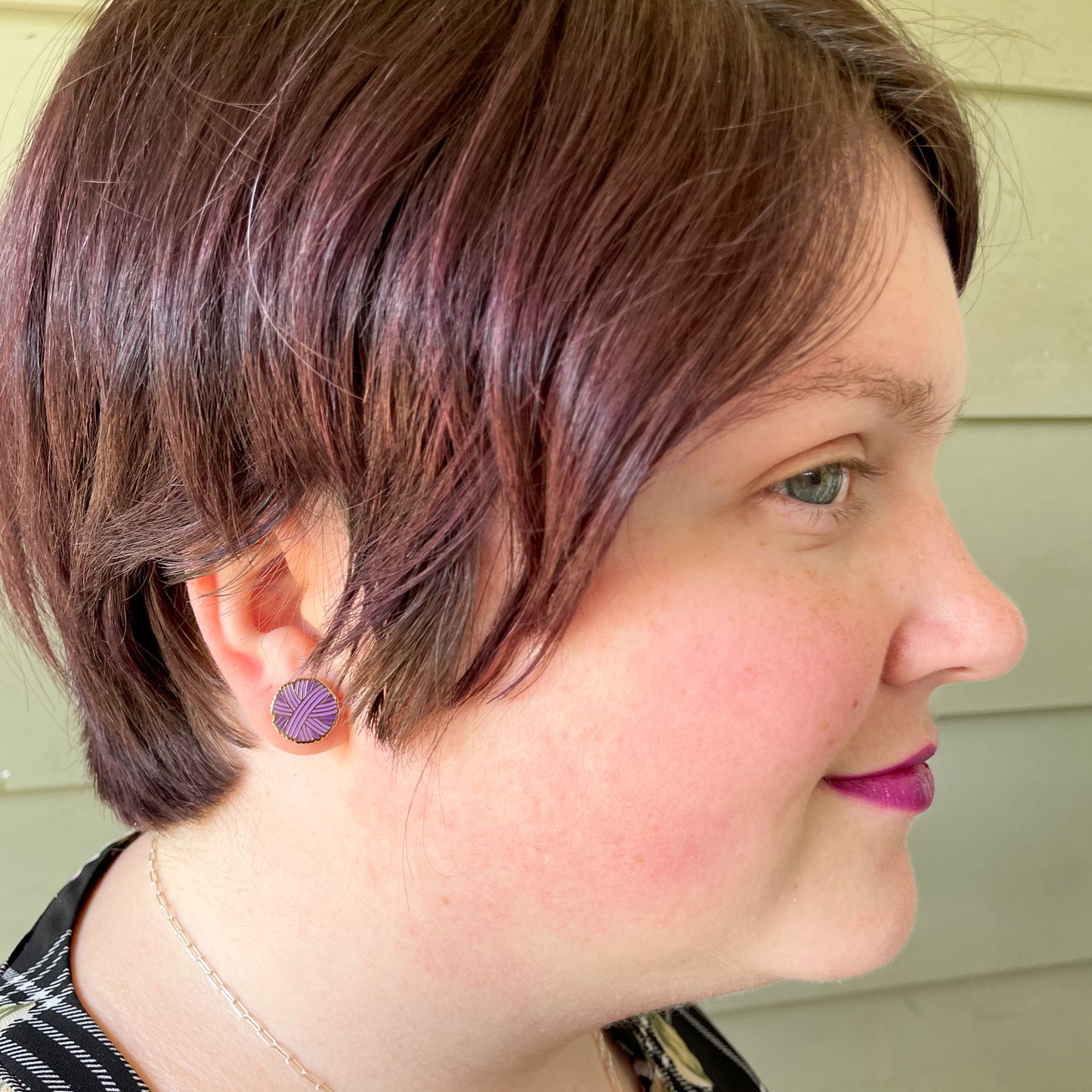A close up of a woman with a short pixie cut wearing a purple yarn ball shaped post earring.