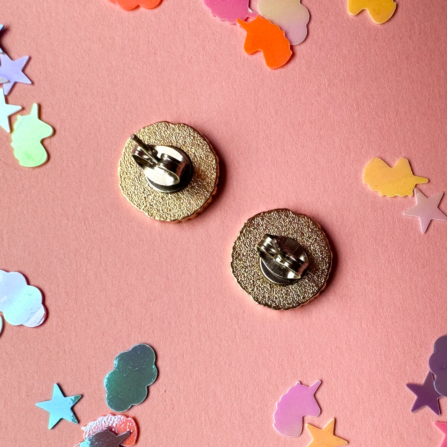 The back of a pair of yarn ball shaped earrings on a pink background
