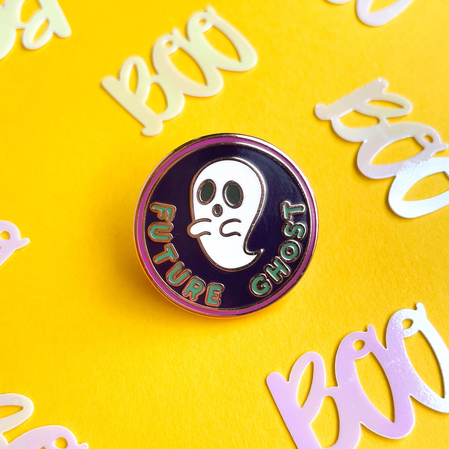 An circular enamel pin with a ghost on it that reads "Future Ghost" on a yellow background.