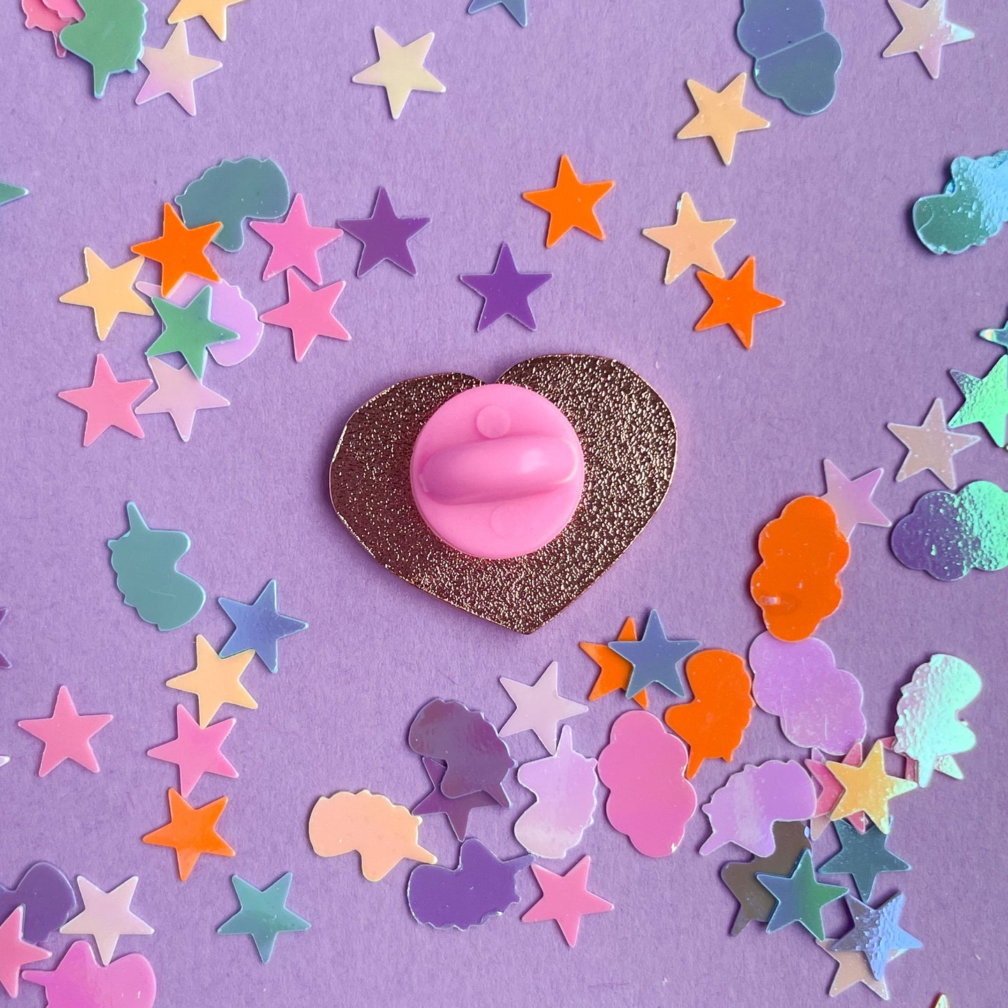 The back of a heart shaped enamel pin with a light pink rubber back.