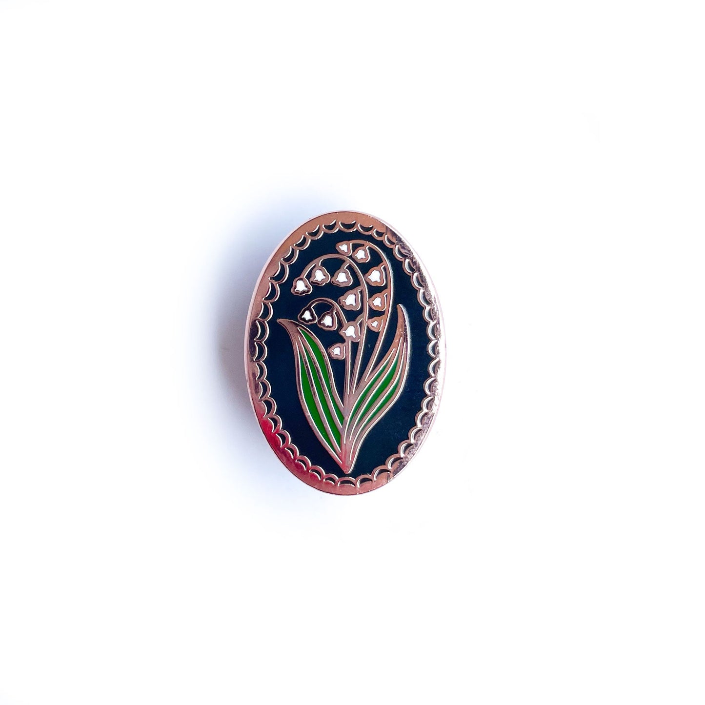 An oval shaped enamel pin with a lily of the valley flower on it.